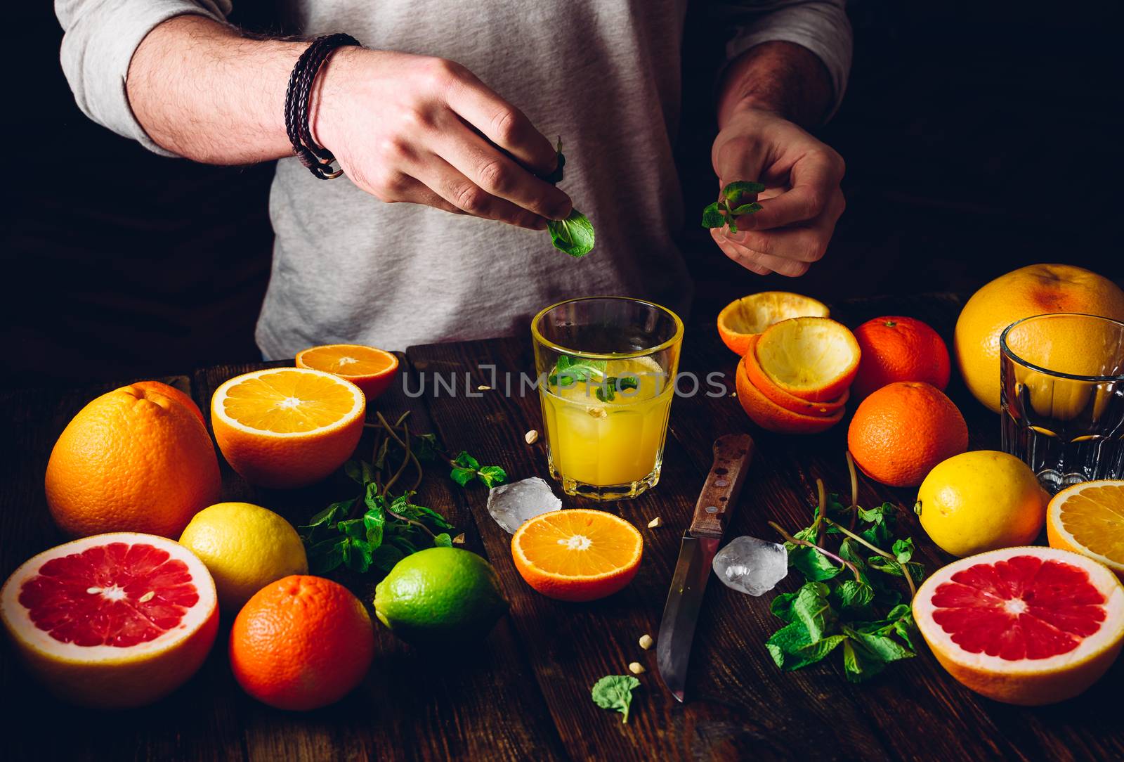 Guy Prepare the Citrus Cocktail with Ice and Mint. Some Ingredients on Table.