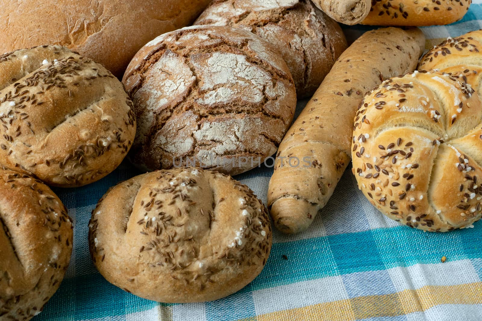 Heap of various bread rolls sprinkled with salt, caraway and sesame. Fresh rustic bread from leavened dough. Assortment of freshly of bakery products