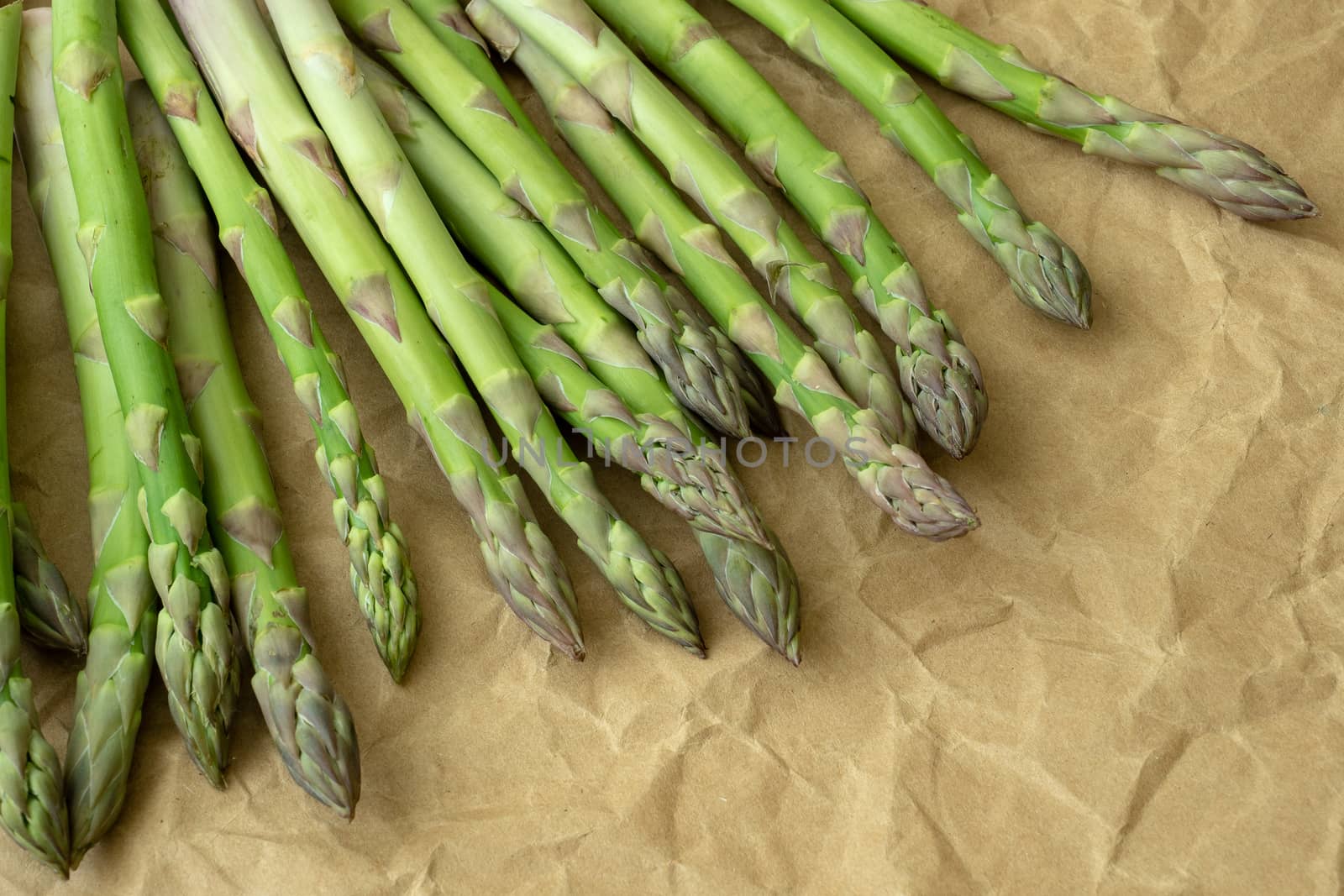Raw garden asparagus stems. Fresh green spring vegetables on brown wrapping paper. (Asparagus officinalis).