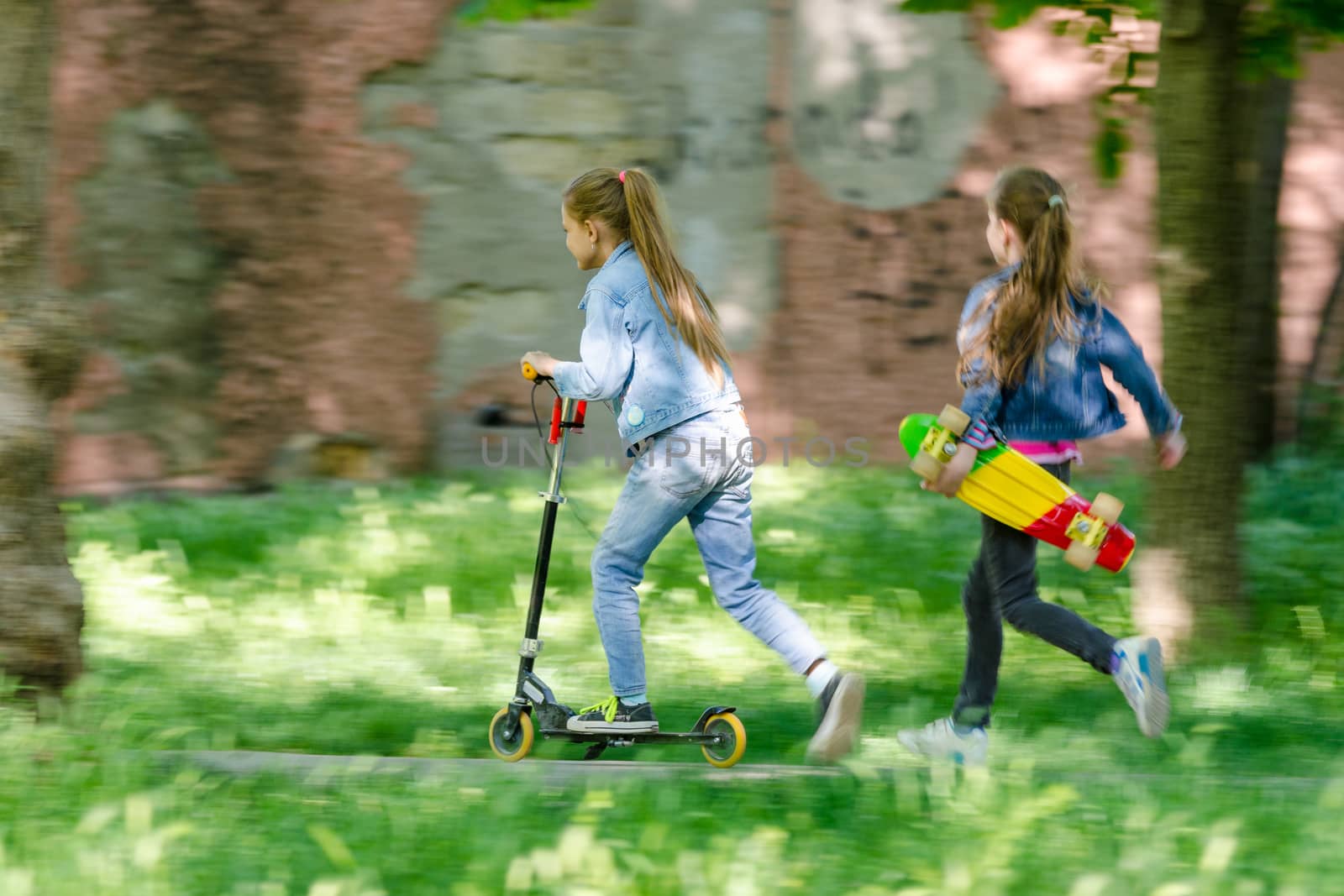 The girl is riding happily on the scooter, behind her runs another girl with a skate in her hands