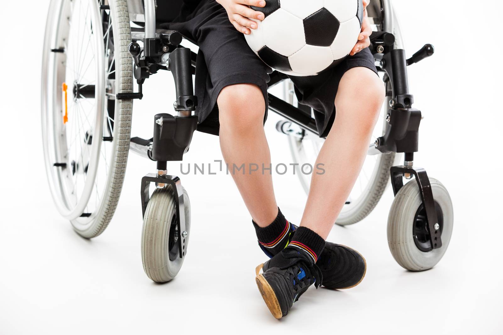 Invalid or disabled child boy sitting on wheelchair hand holding soccer sport ball white isolated