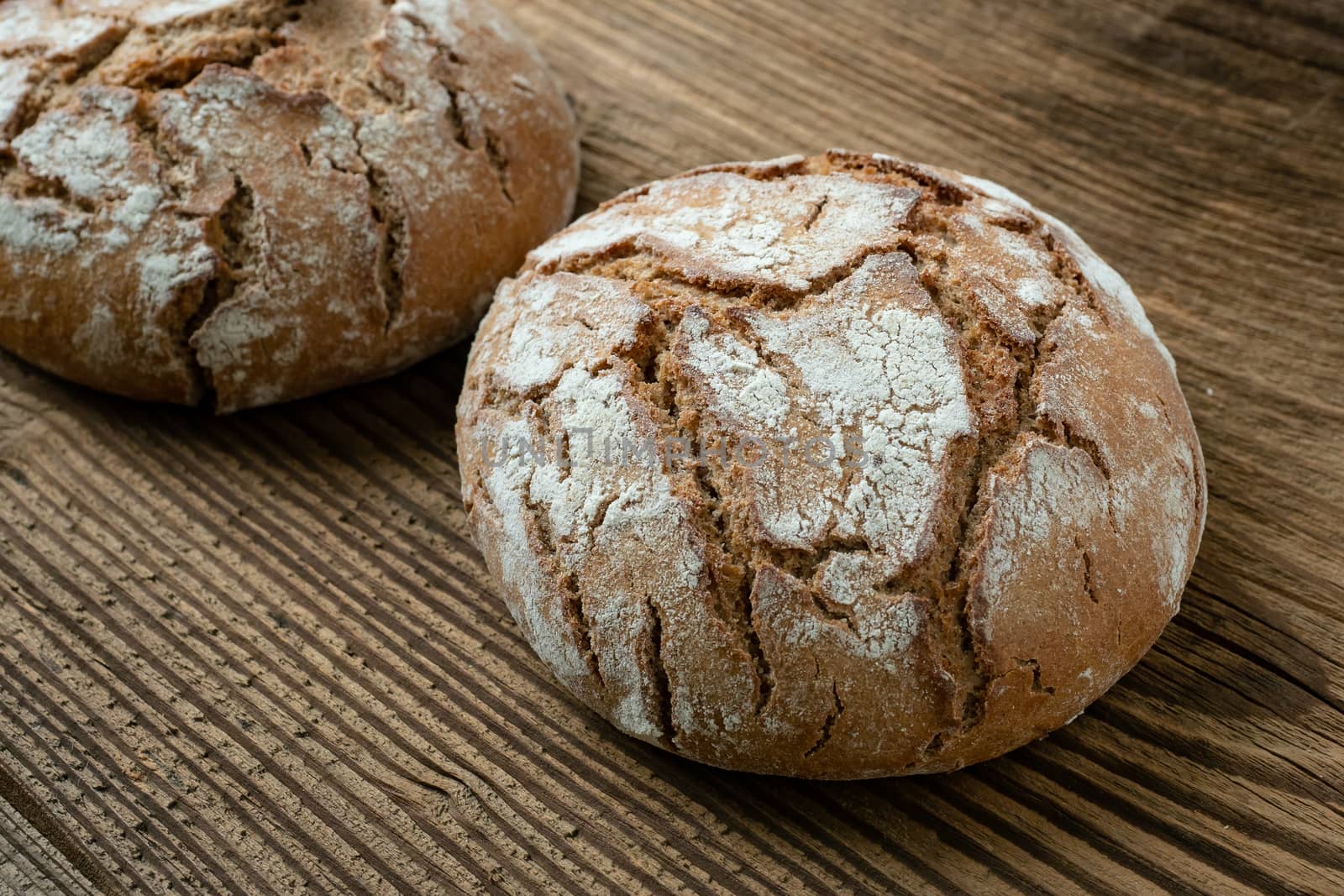 A freshly baked rustic, loaf of bread on an old wooden table by xtrekx