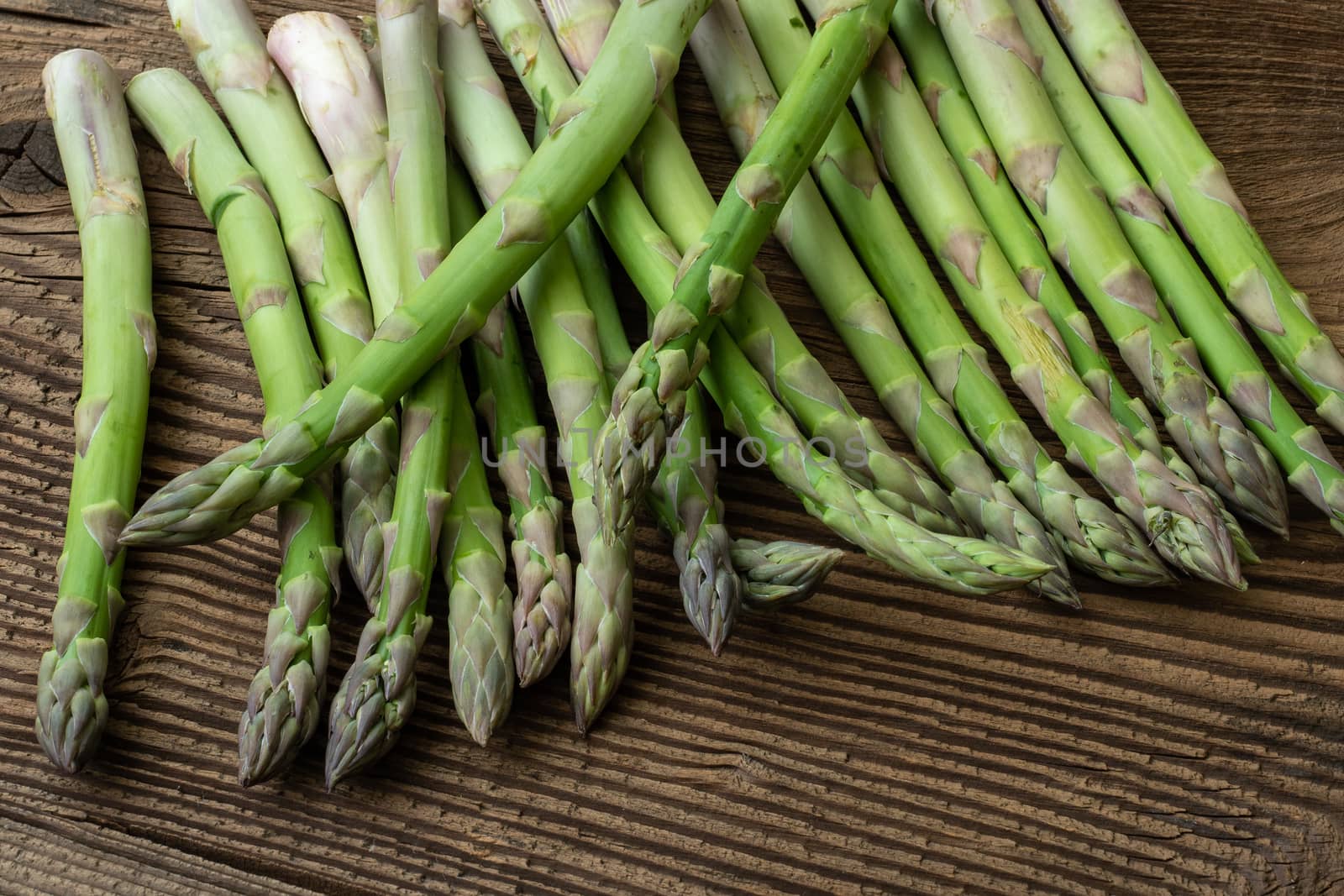 Raw garden asparagus stems. Fresh green spring vegetables on wooden background. (Asparagus officinalis).