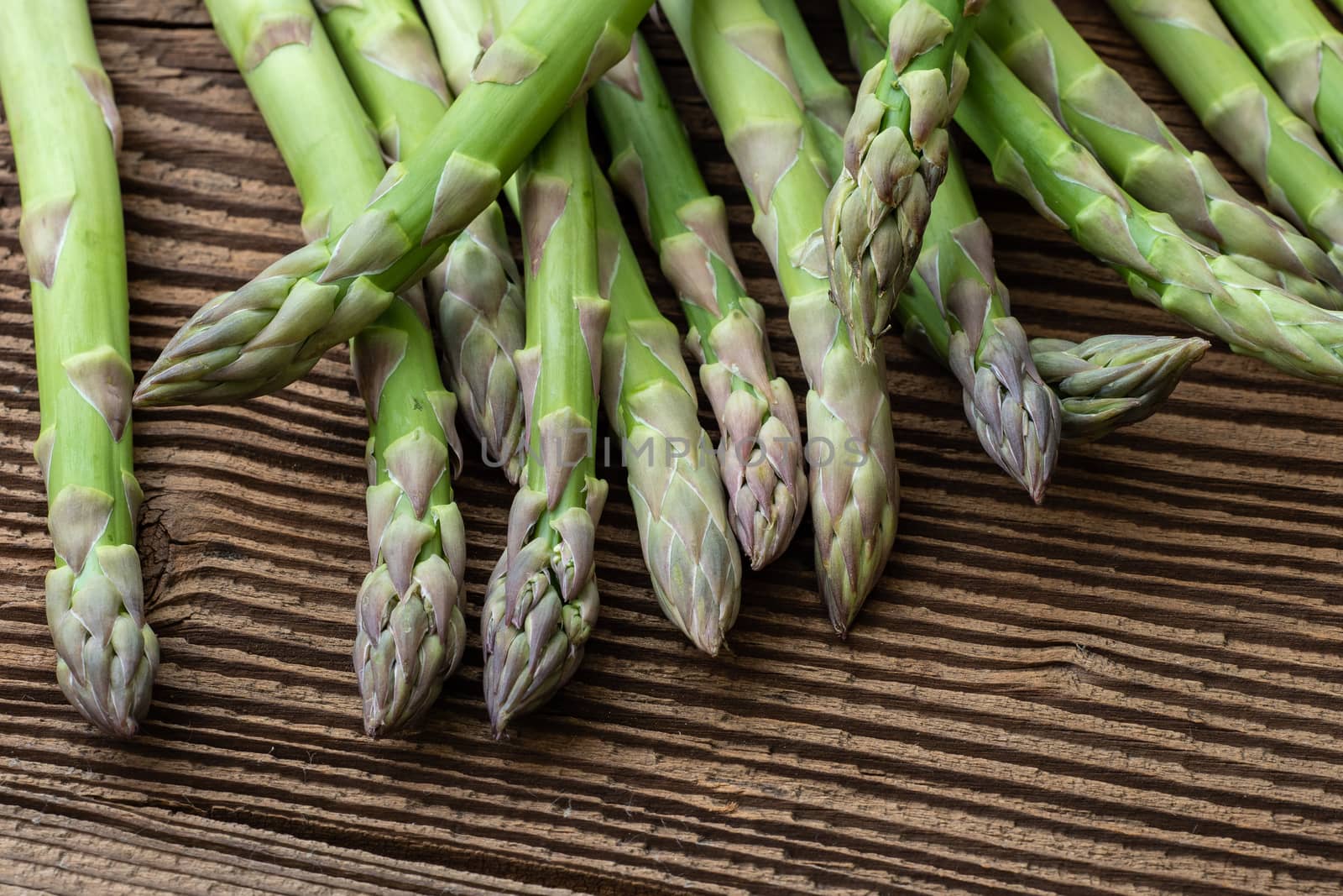 Raw garden asparagus stems. Fresh green spring vegetables on wooden background. (Asparagus officinalis).
