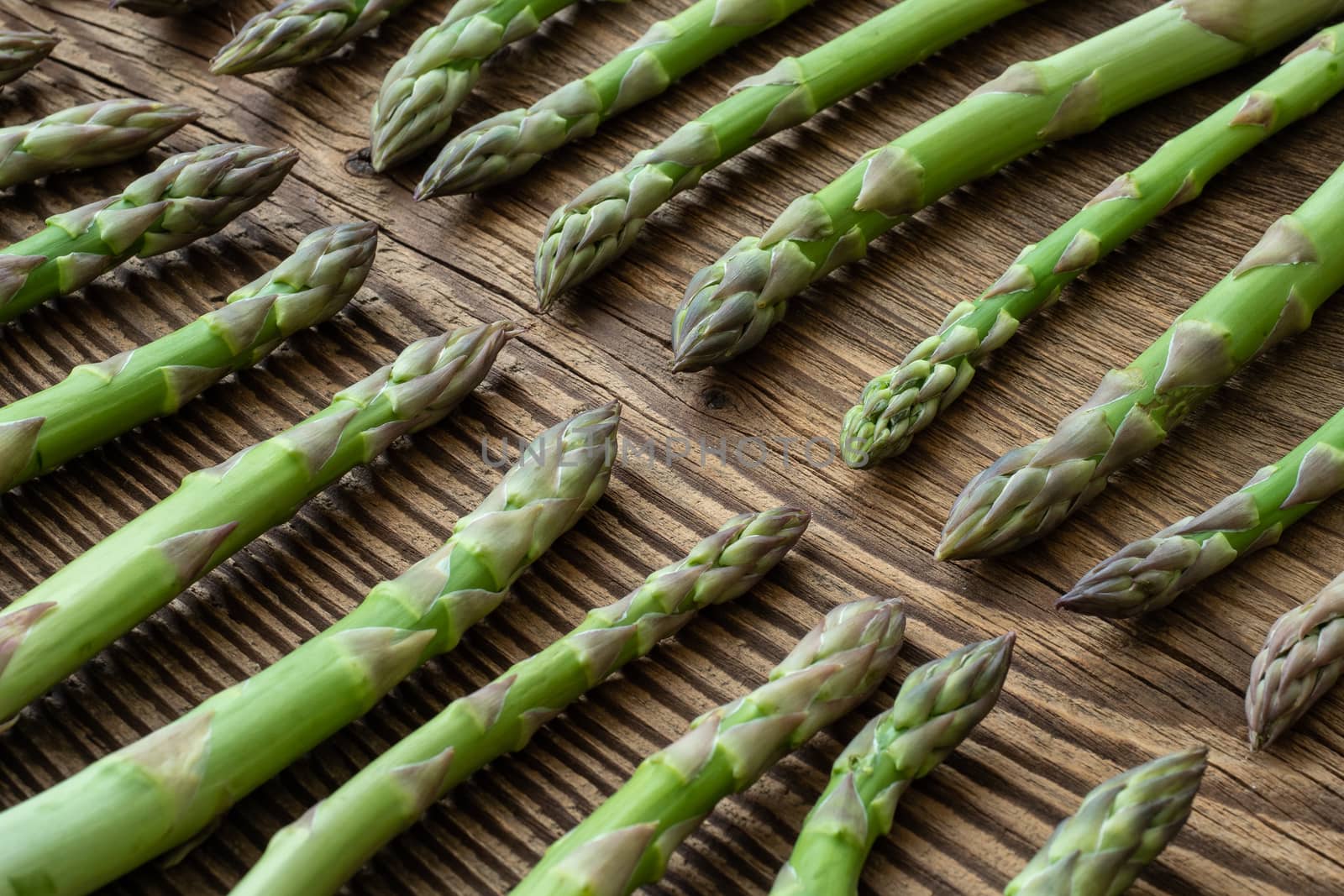 Raw garden asparagus stems. Fresh green spring vegetables on wooden background. (Asparagus officinalis).