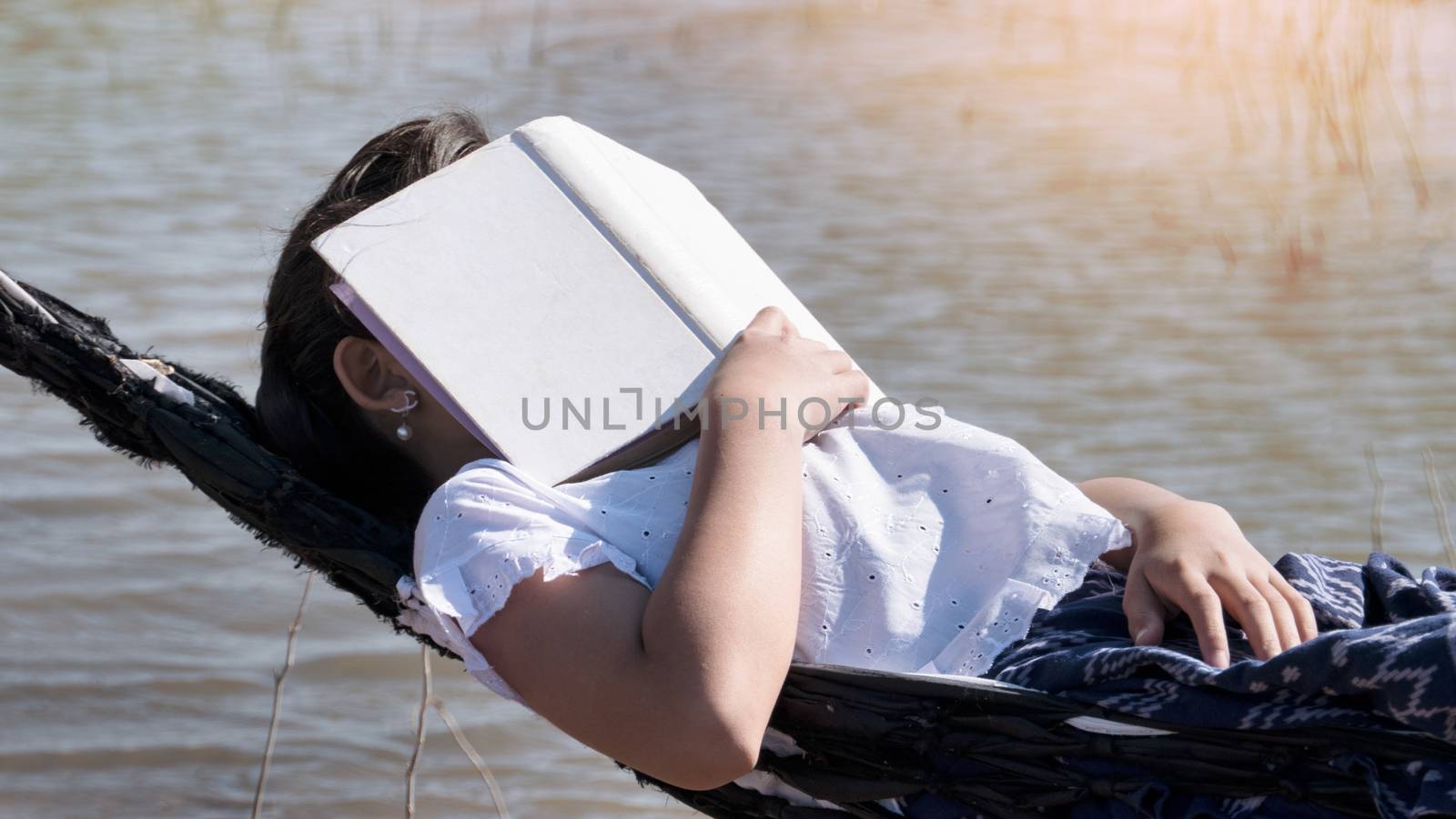 Close up of young beautiful girl sleeping in a hammock and holding a book with her hands