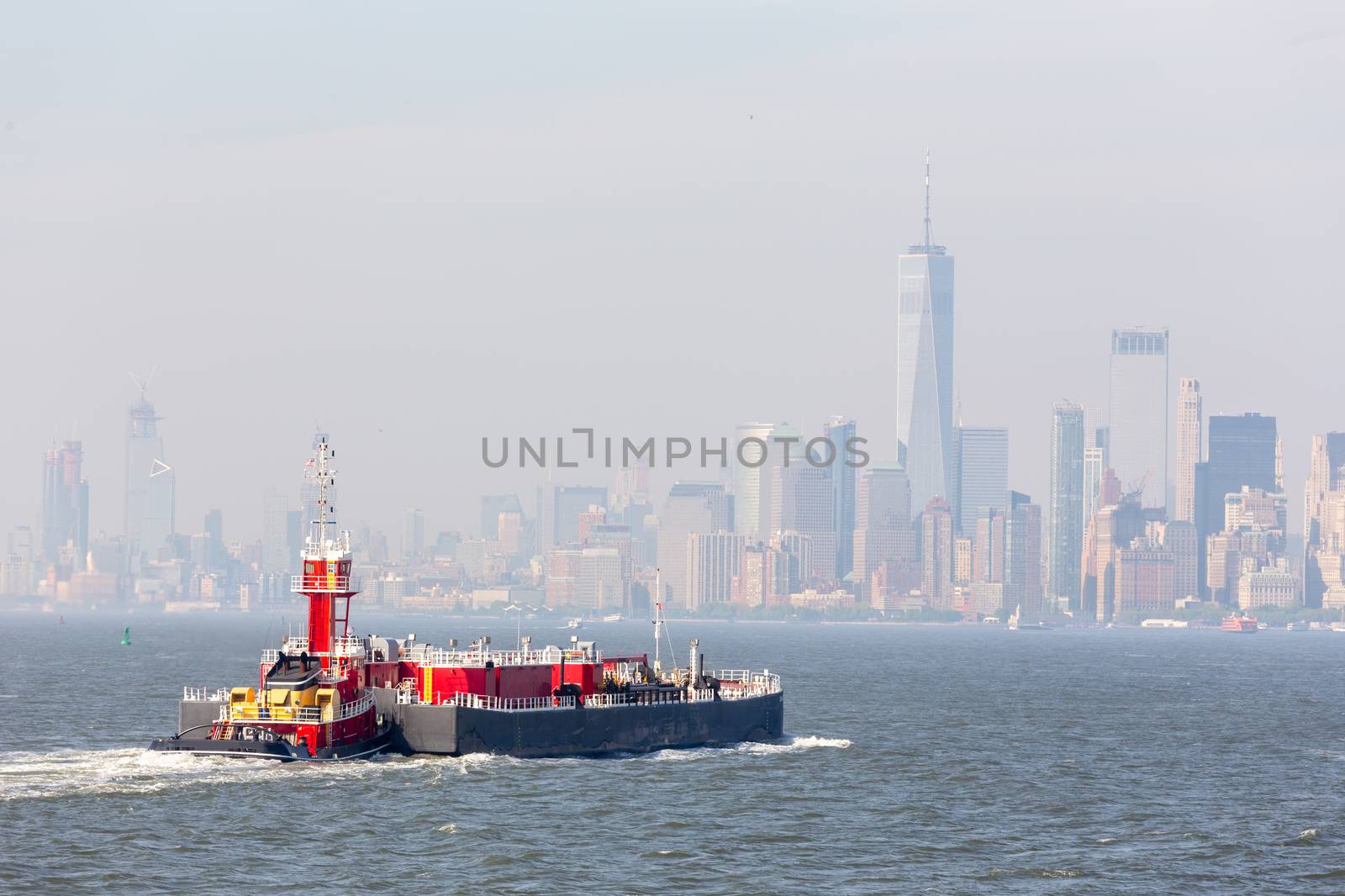 Freight tug pushing cargo ship to the port in New York City and Lower Manhattan skyscarpers skyline in background. by kasto