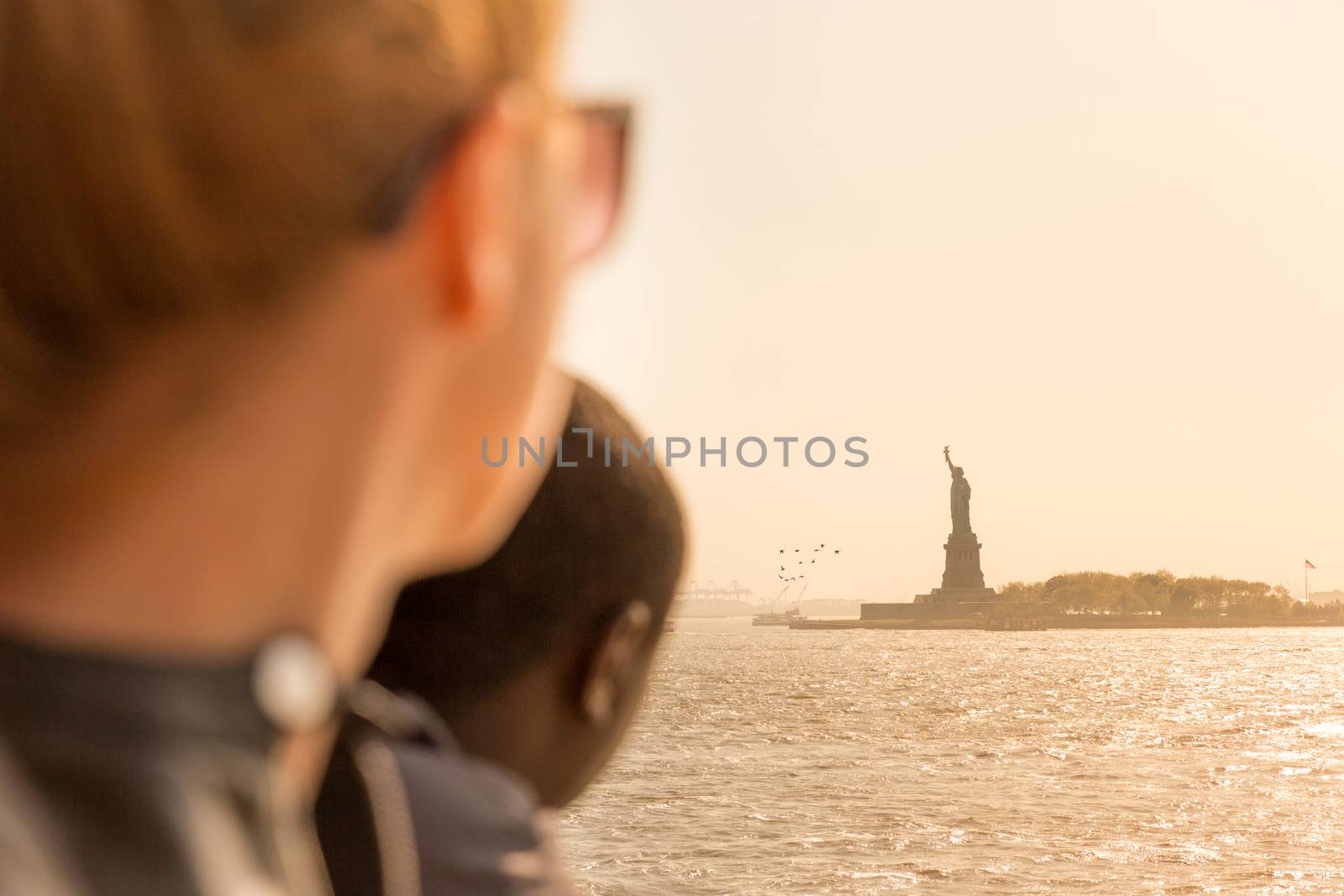 Tourists looking at Statue of Liberty silhouette in sunset from the staten island ferry, New York City, USA by kasto