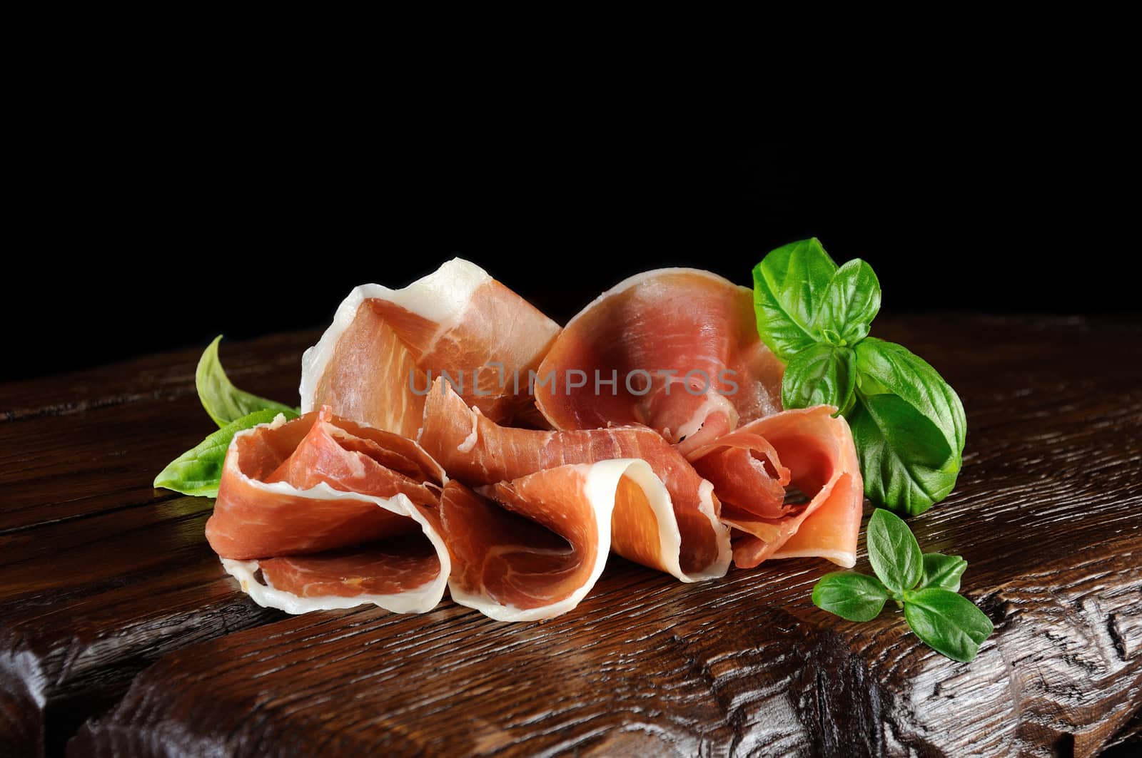 parma ham (jamon) sliced and basil on a wooden board.