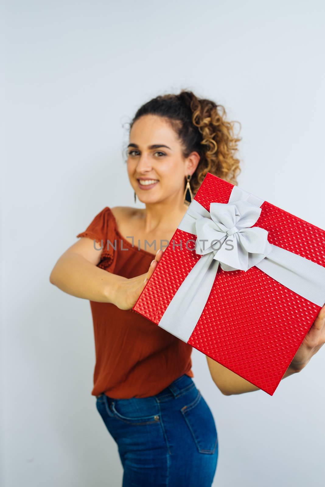 Attractive Curly Long Haired Woman Is Holding A Gift Box With Ribbon Isolated On White Background