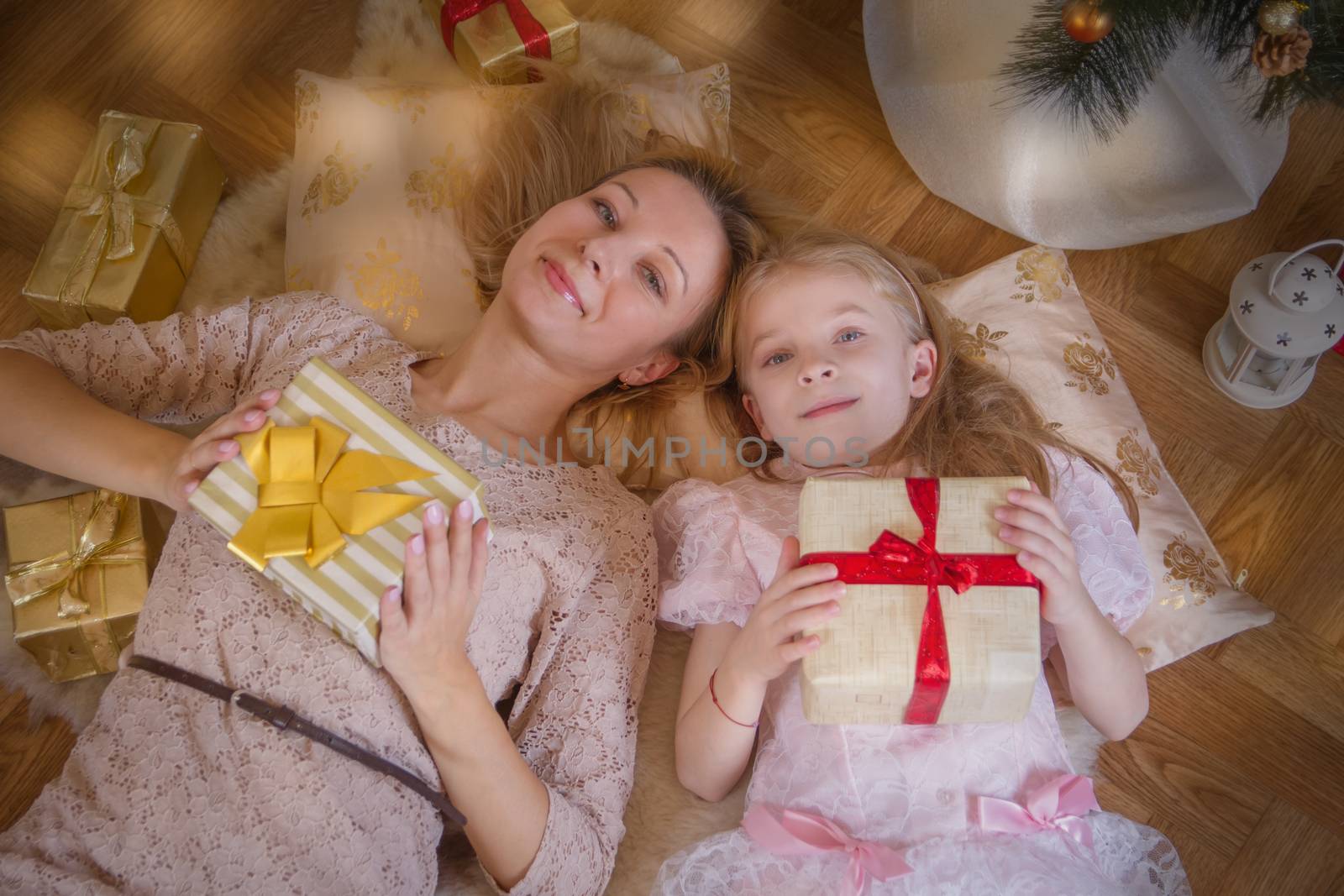 Mother and daughter lying with gifts under Christmas tree by Angel_a