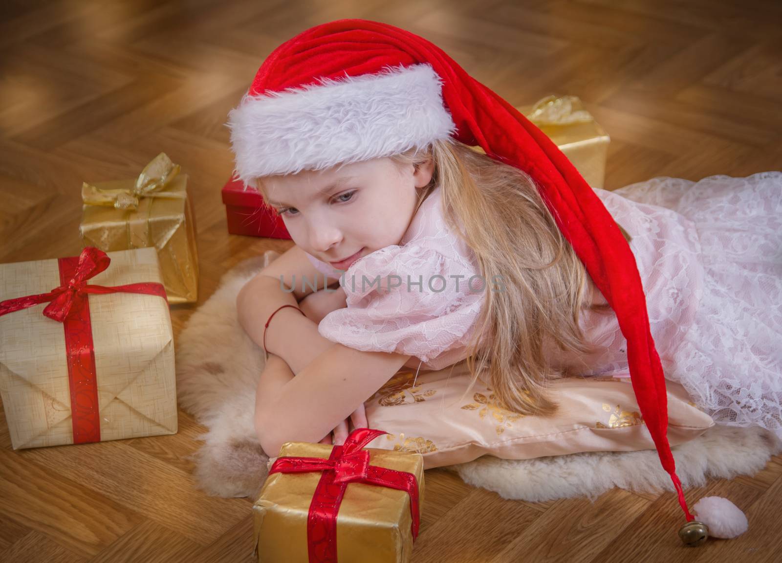 Cutre girl in Santa hat lying among Christmas gifts