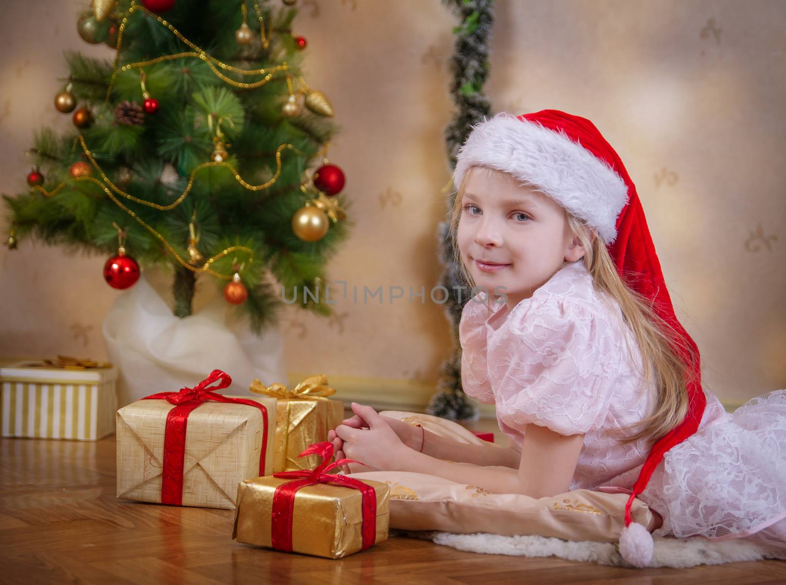 Girl in Santa hat dreaming under Christmas tree with gifts by Angel_a