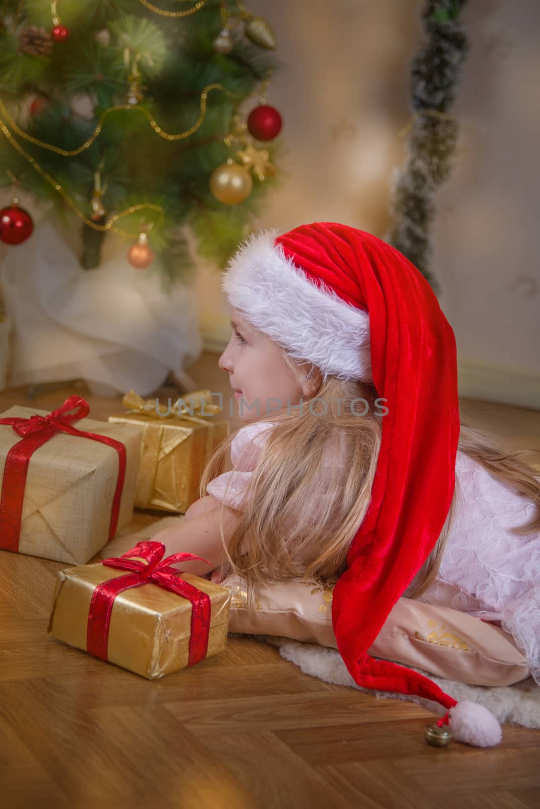 Girl in Santa hat dreaming under Christmas tree with gifts by Angel_a