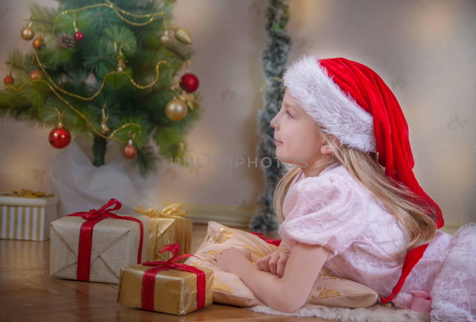 Cute girl in Santa hat dreaming under Christmas tree