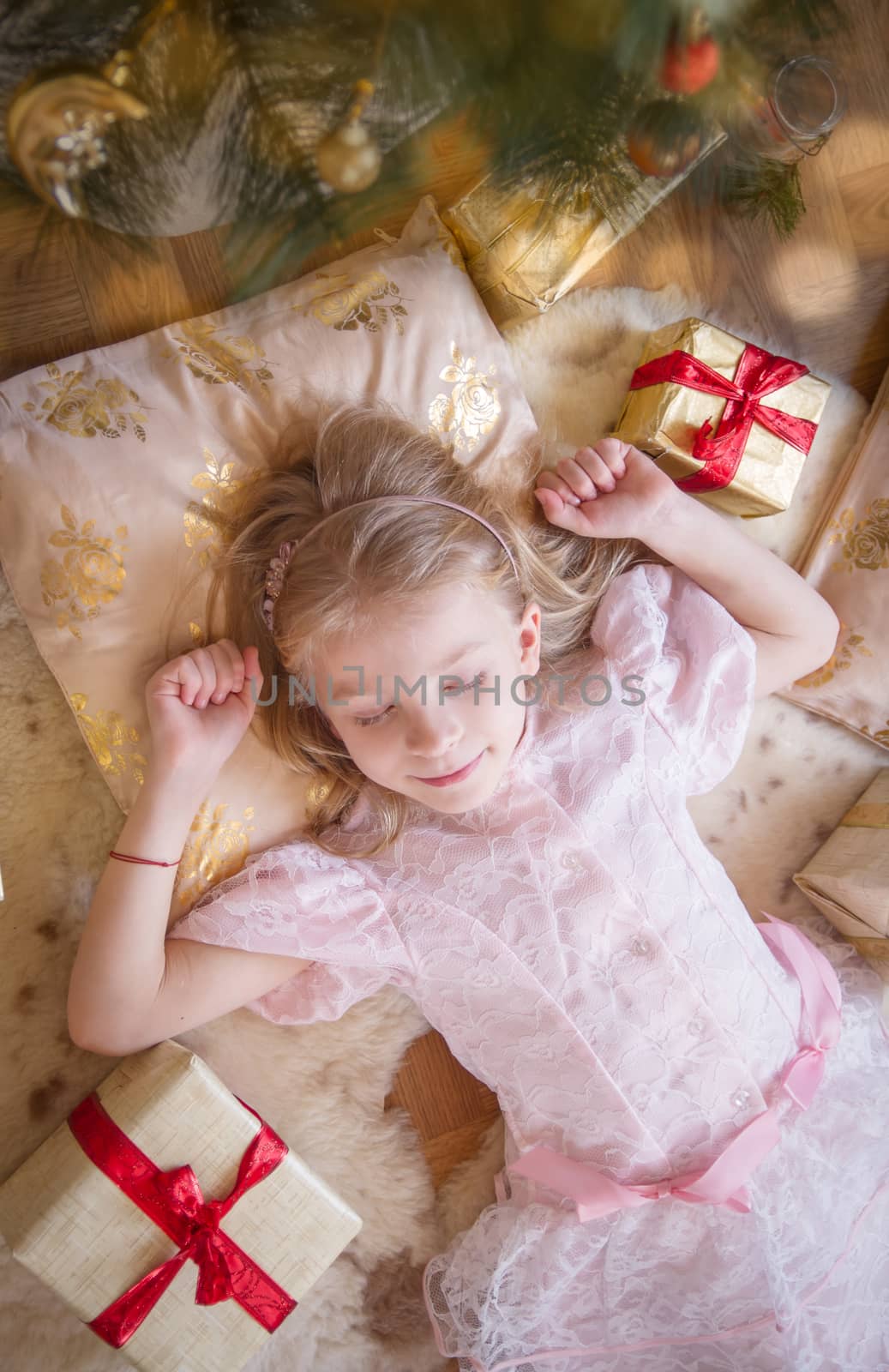 Cute girl dreaming under Christmas tree with gifts, top view