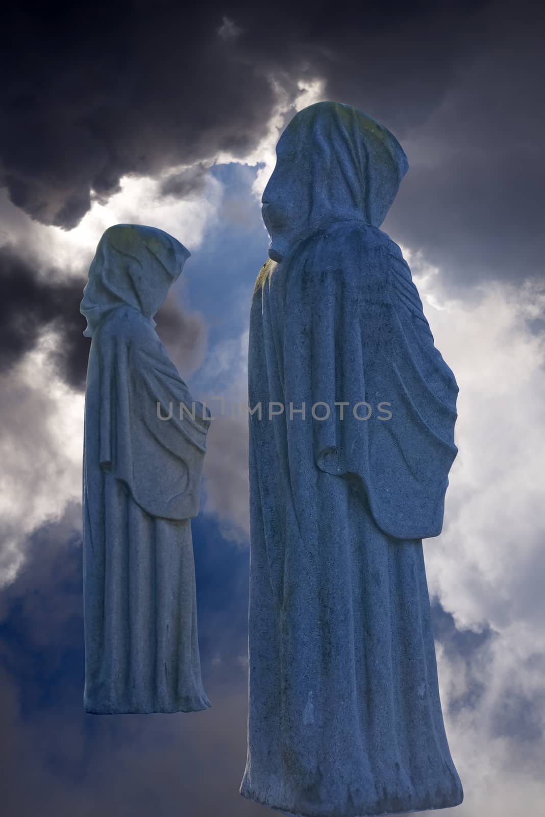two faceless monk statues against dark skies by morrbyte