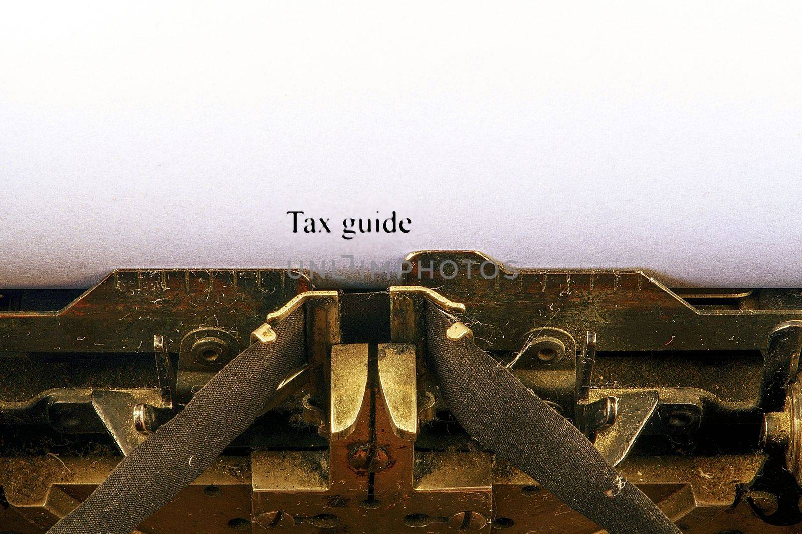 Closeup on vintage typewriter. Front focus on letters making TAX GUIDE text. Business concept image with retro office tool.