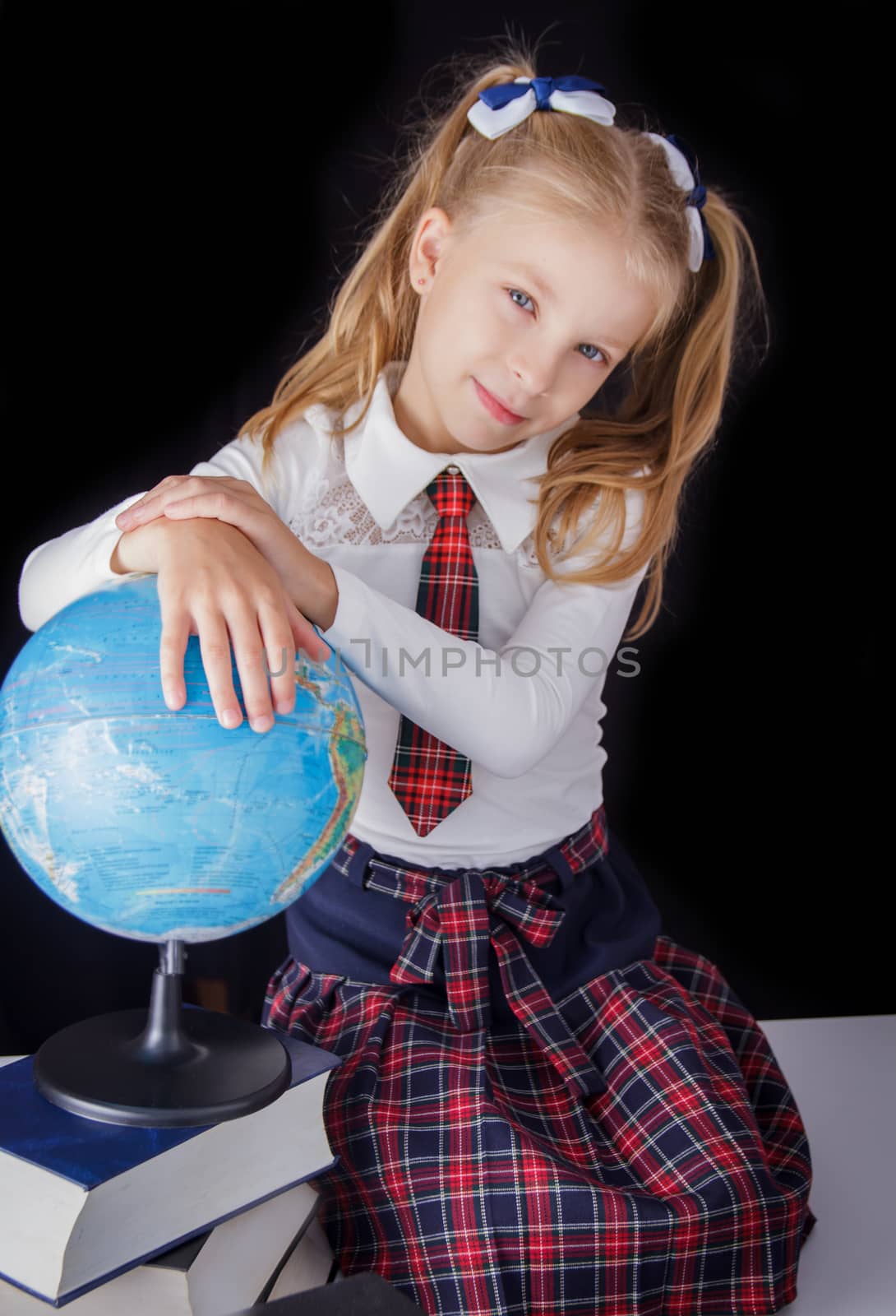 Schoolgirl with globe sitting on black background, education and school concept