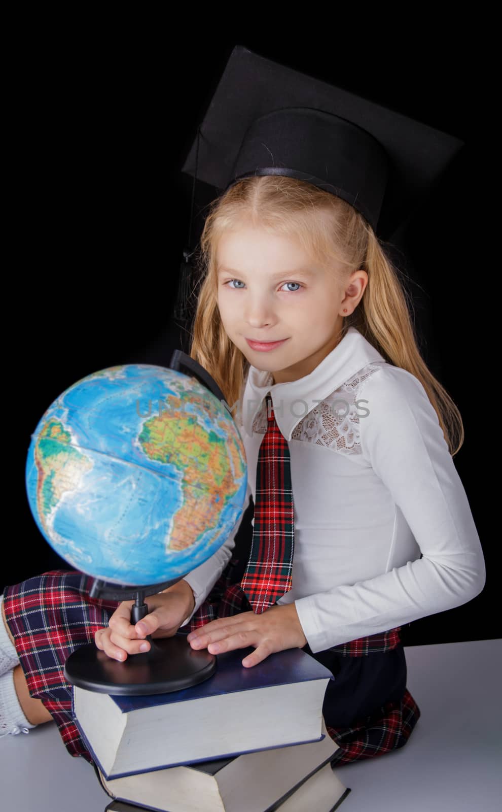 Schoolgirl with hat and globe sitting on black background, education and school concept