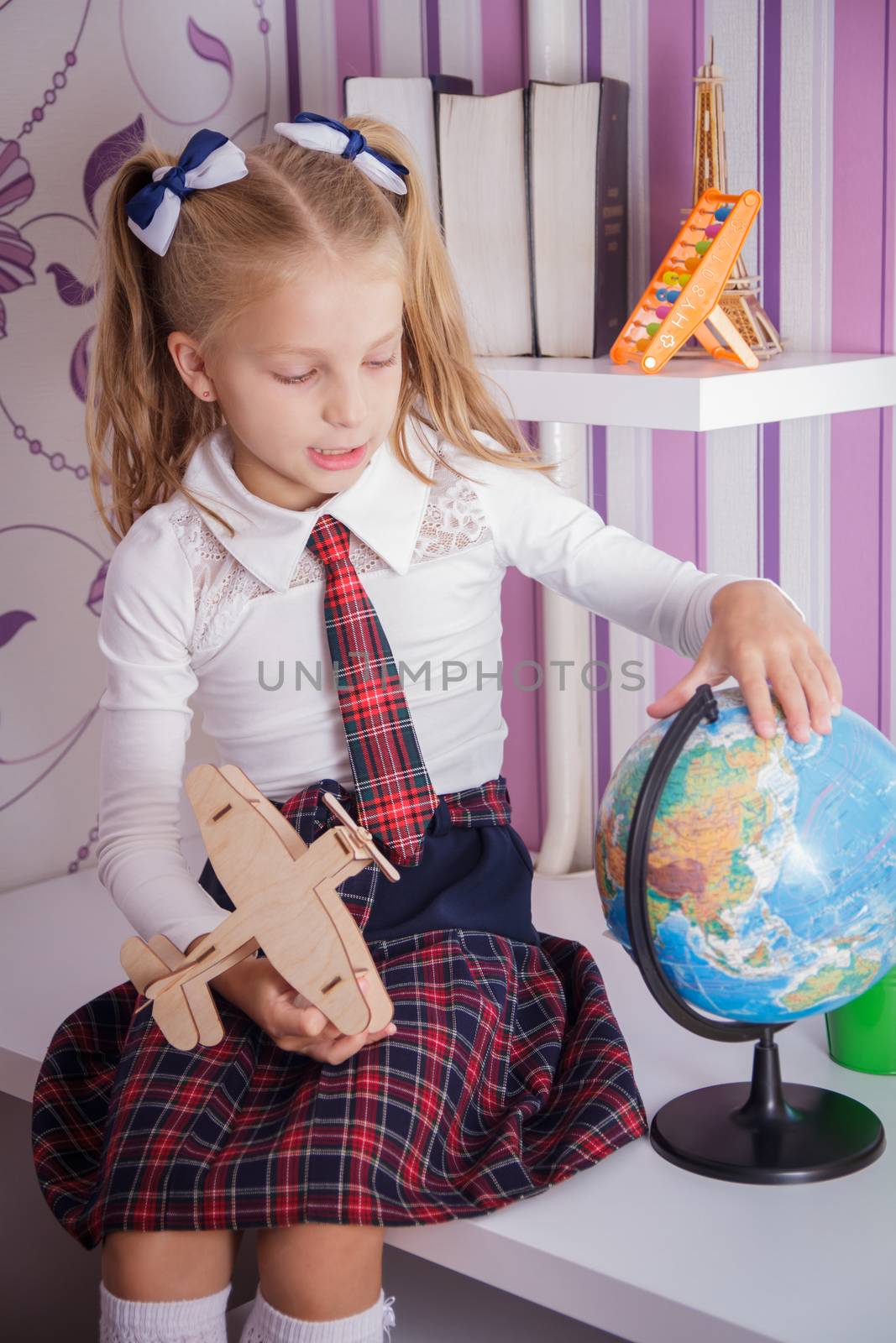 Cute schoolgirl with globe sitting on table, education and travel concept