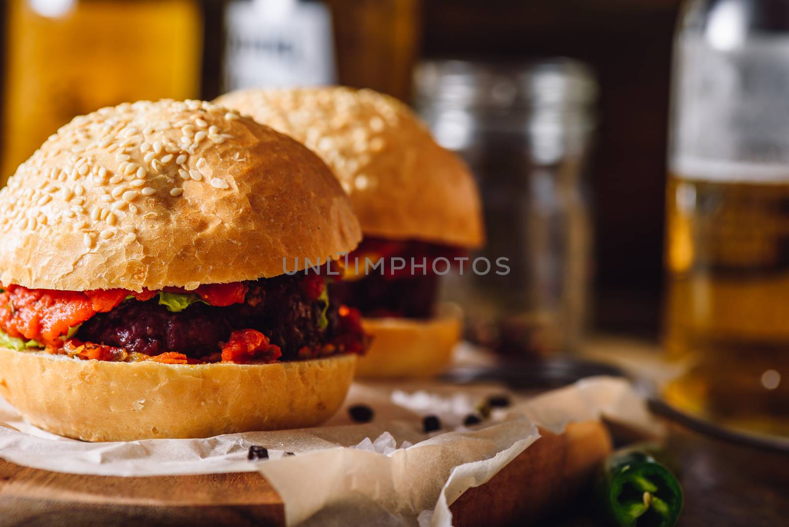 Burger on Cutting Board with Some Ingredients and Beer Bottle on Backdrop.