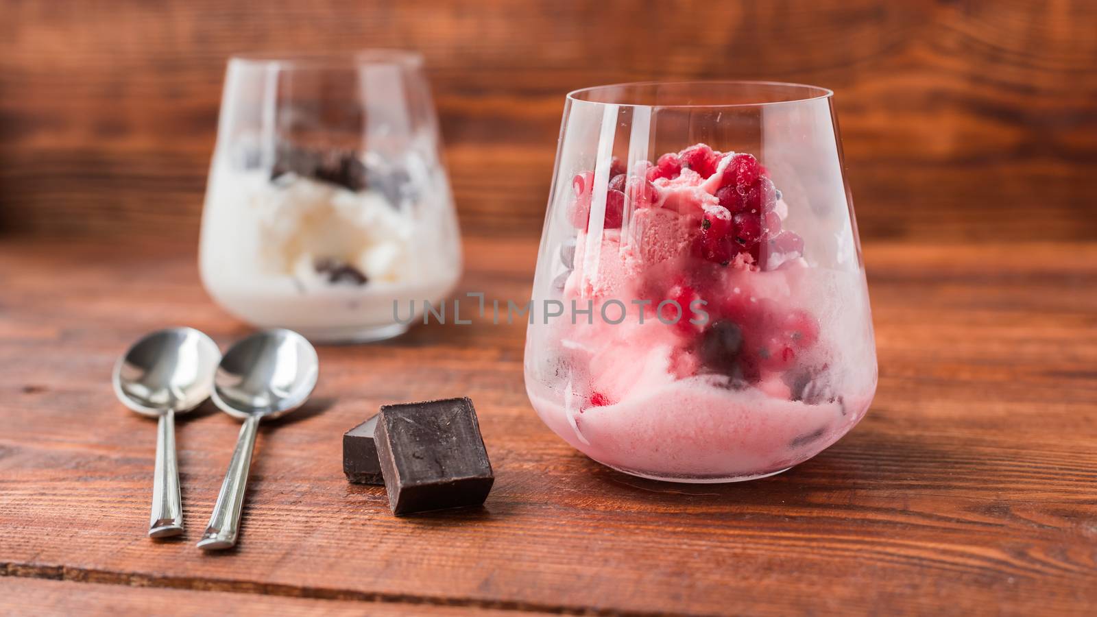 White and pink ice cream in glass on wooden table. Sweet desert