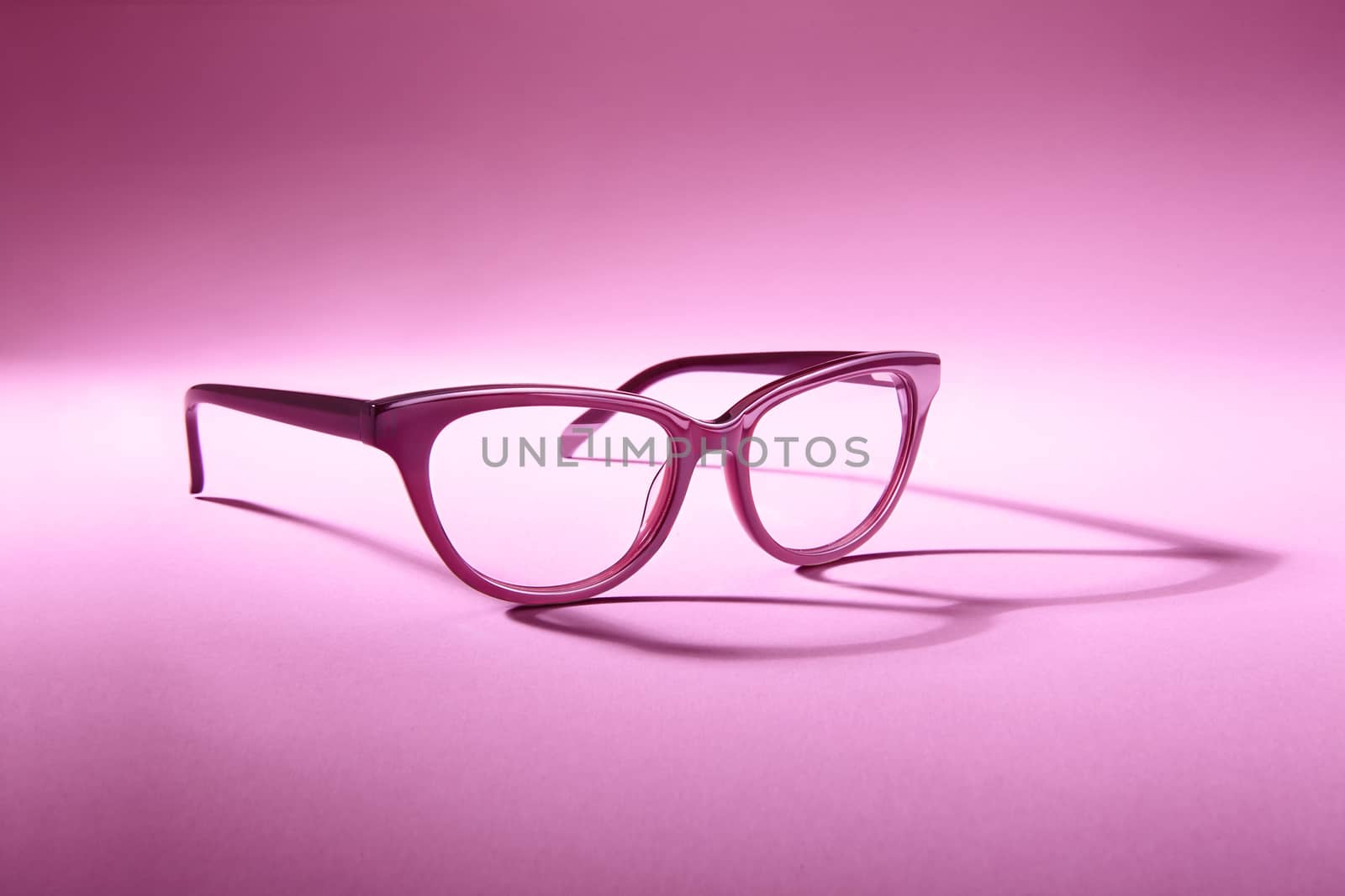 Advertising studio shot of pink glasses with long shadow at pink background.