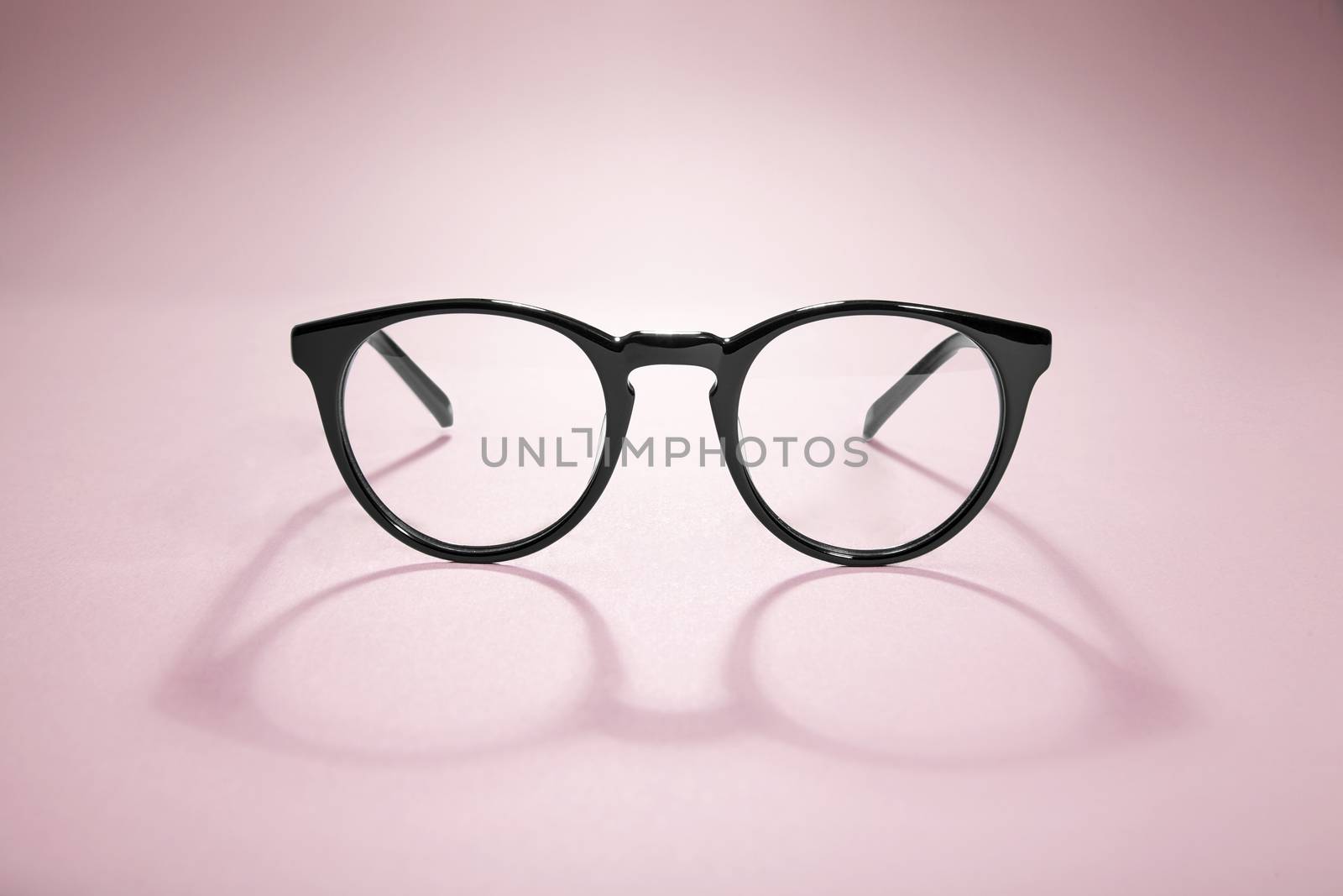 Studio shot of black glasses with long shadow at pink background.