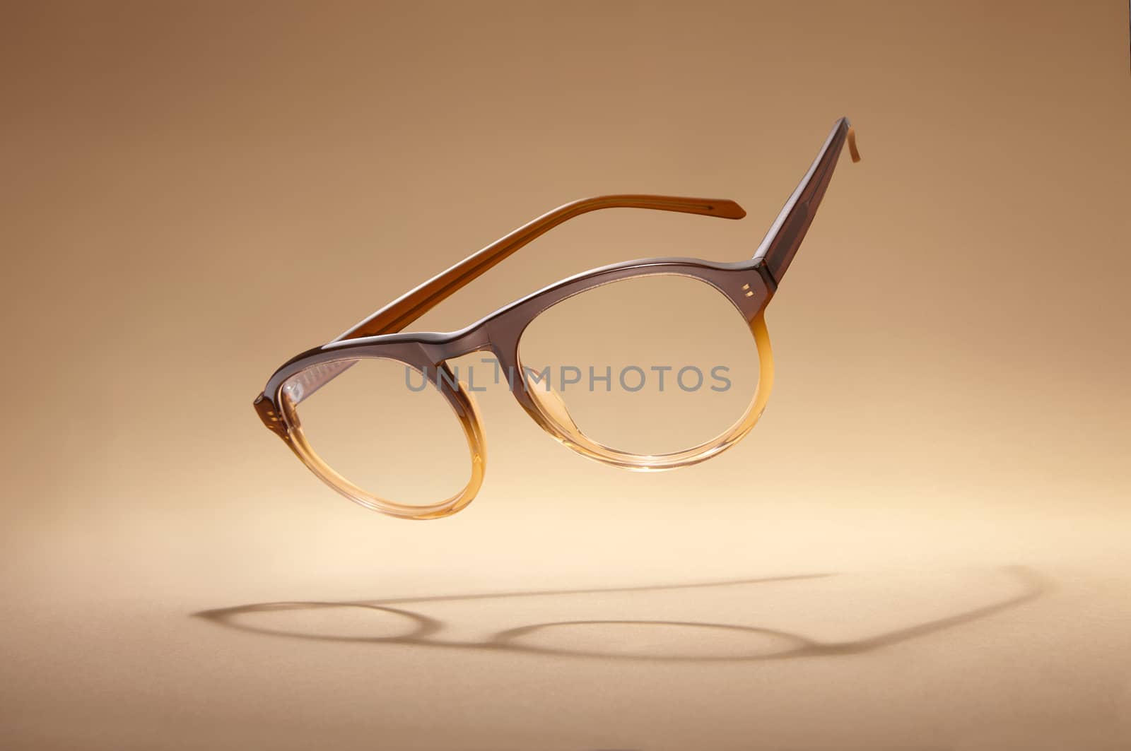 Studio shot of flying brown glasses with shadow on beige background.