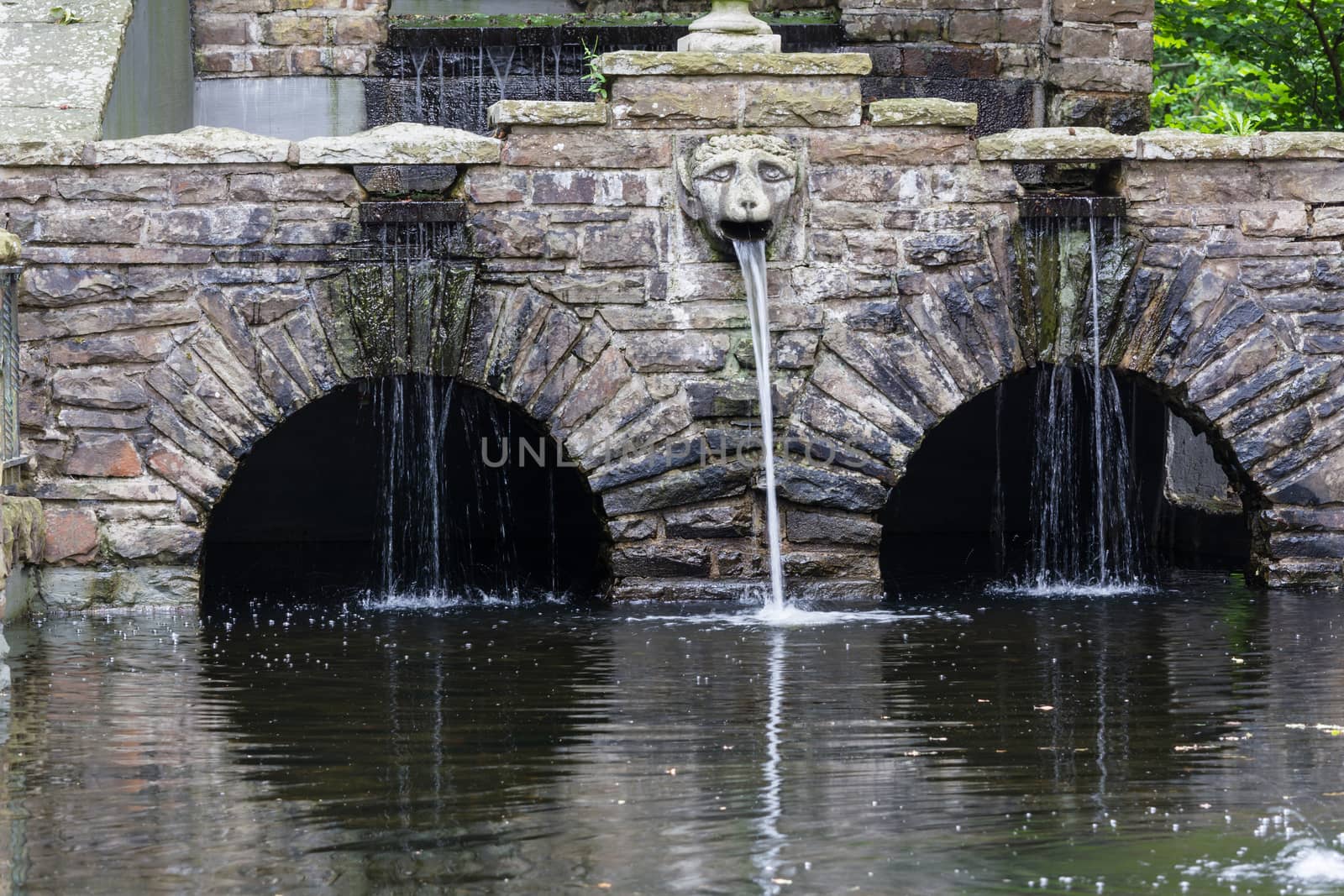 Fountain with waterfall with rock stone decoration in the garden or park. Landscape design detail.