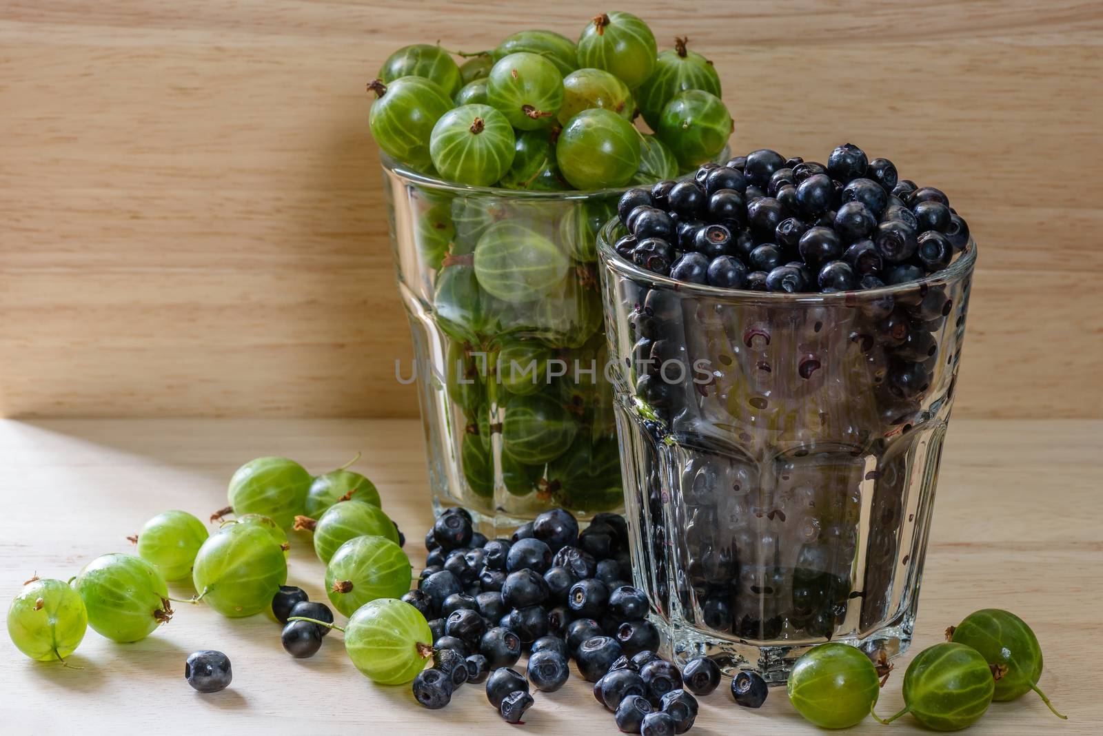 Blueberries and gooseberries in glass with scattered berries. by Seva_blsv