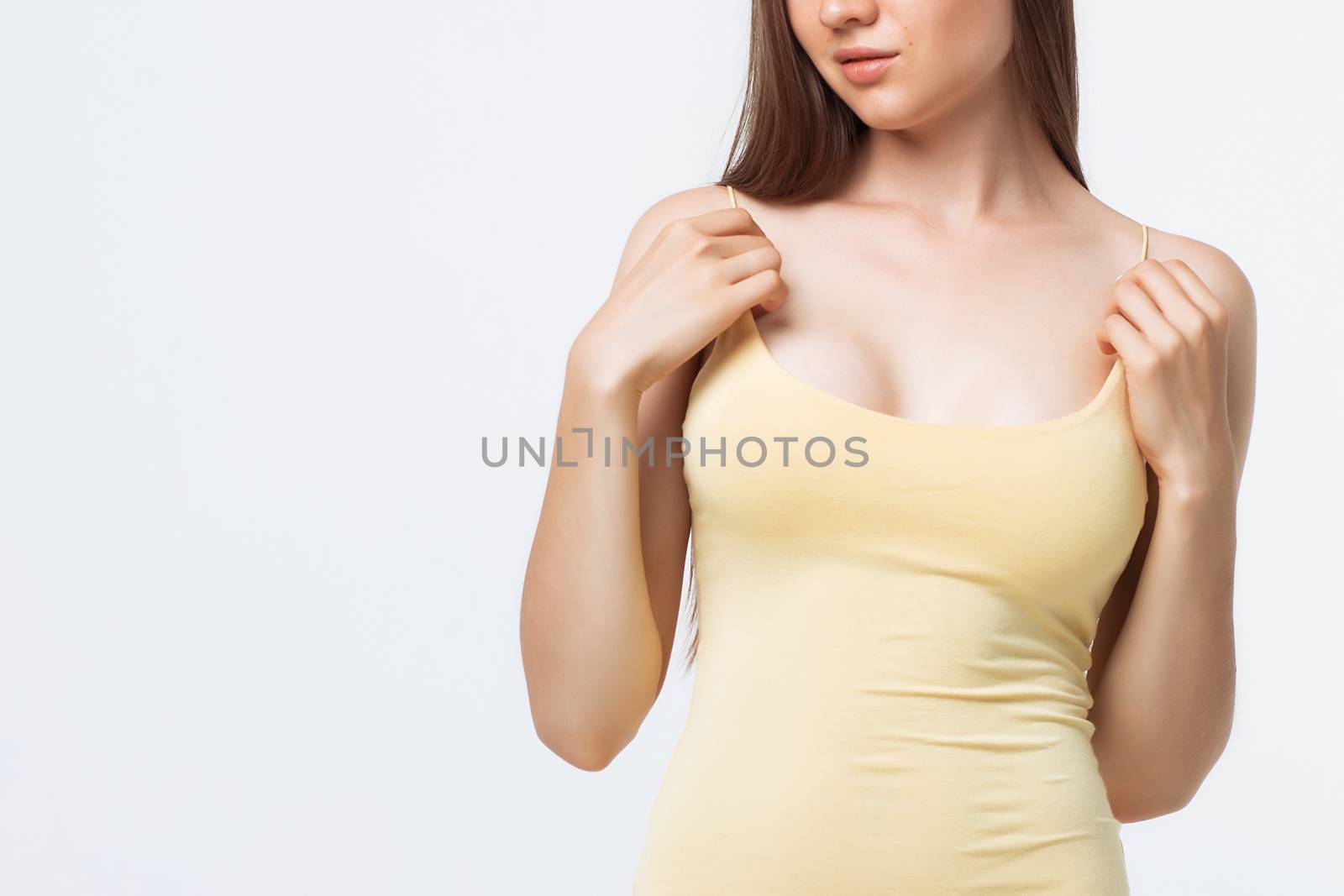Sensual young female in lingerie creasing tank top and looking away while standing on white background