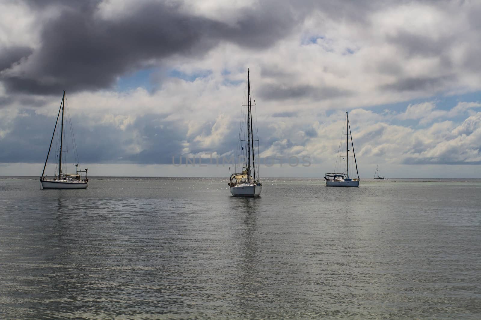 three sail boat on the ocean during a cloudy day