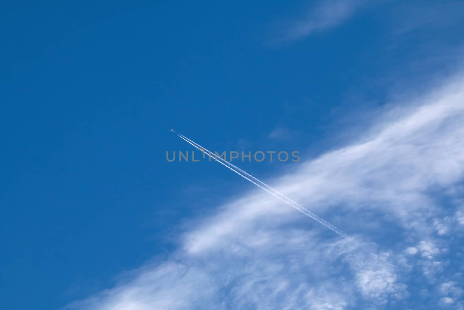 Plane, contrail and Cirrocumulus Clouds against blue sky.