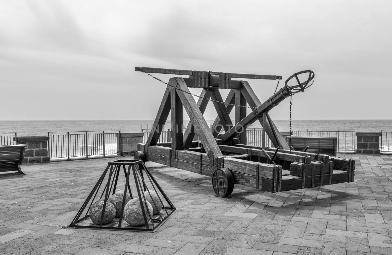 ancient catapult on the ramparts of Alghero ,Sardinia Island, Italy , Defensive wall. Catapult in the downtown of the citywith the sea as background and the big stone bullets in front