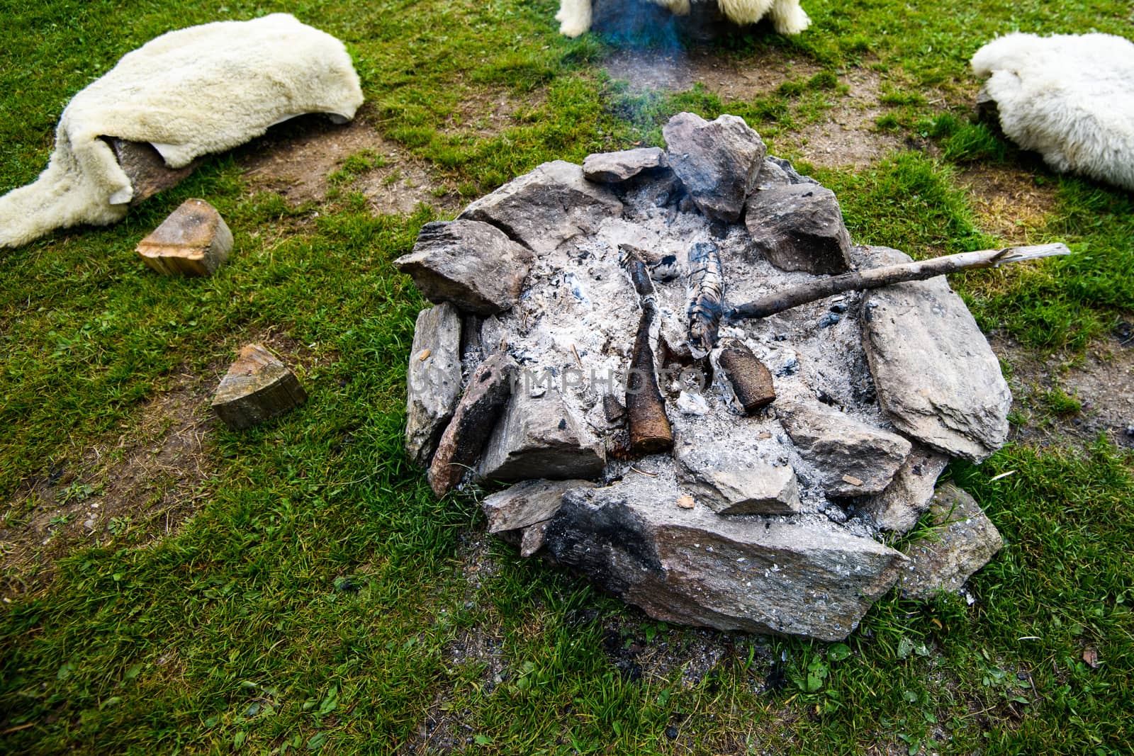 Camp fire made of stone ring, traditional, authentic camp fire of Alpine herders, next to the fire are logs covered in sheep skin