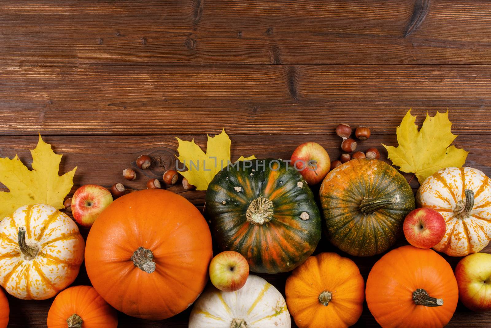 Autumn harvest still life with pumpkins, apples, hazelnut and maple leaves on wooden background