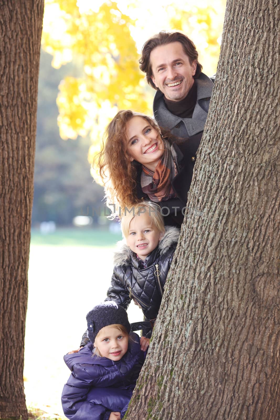 Happy smiling family of parents and children in autumn park standing near big tree trunk