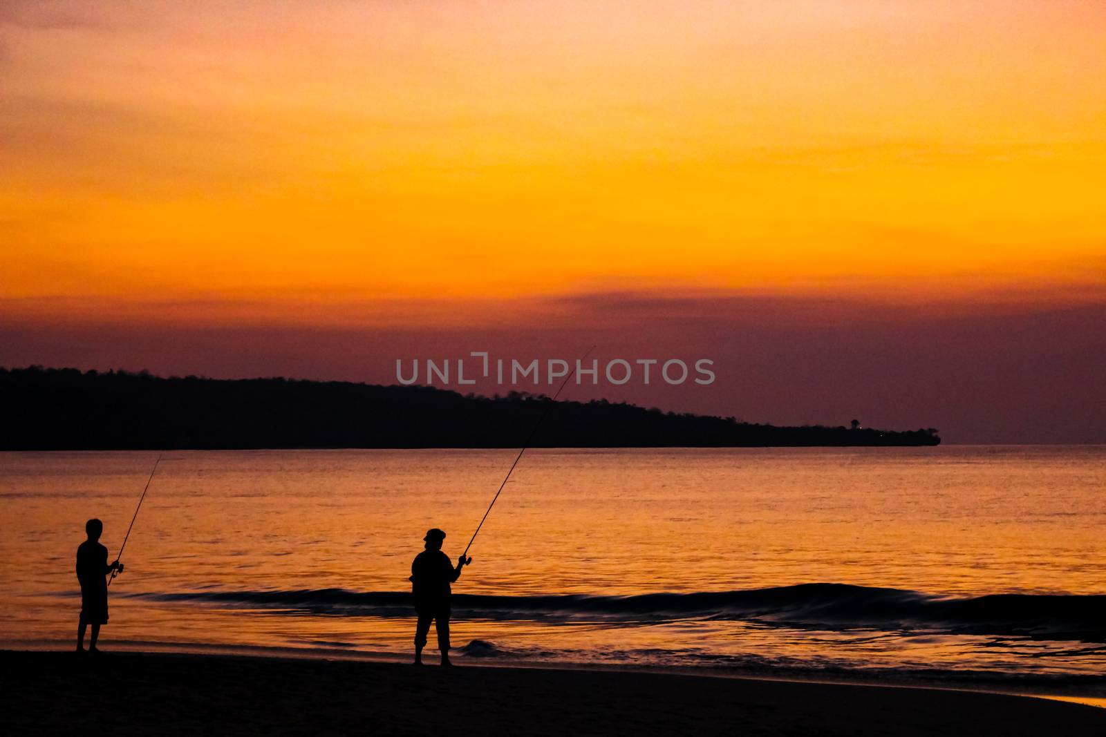 Fishermen catch fish on fishing rods on the beach against the bright sunset. Bali, Indonesia.