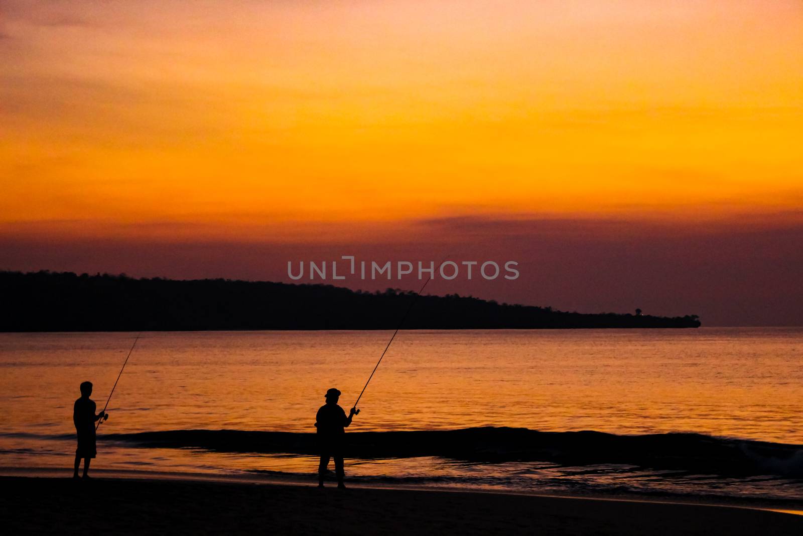 Fishermen catch fish on fishing rods on the beach against the bright sunset. Bali, Indonesia.