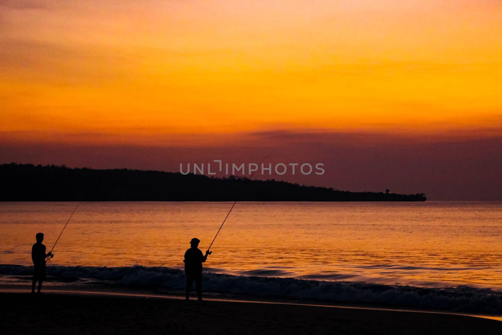 Fishermen catch fish on fishing rods on the beach against the bright sunset. Bali, Indonesia.