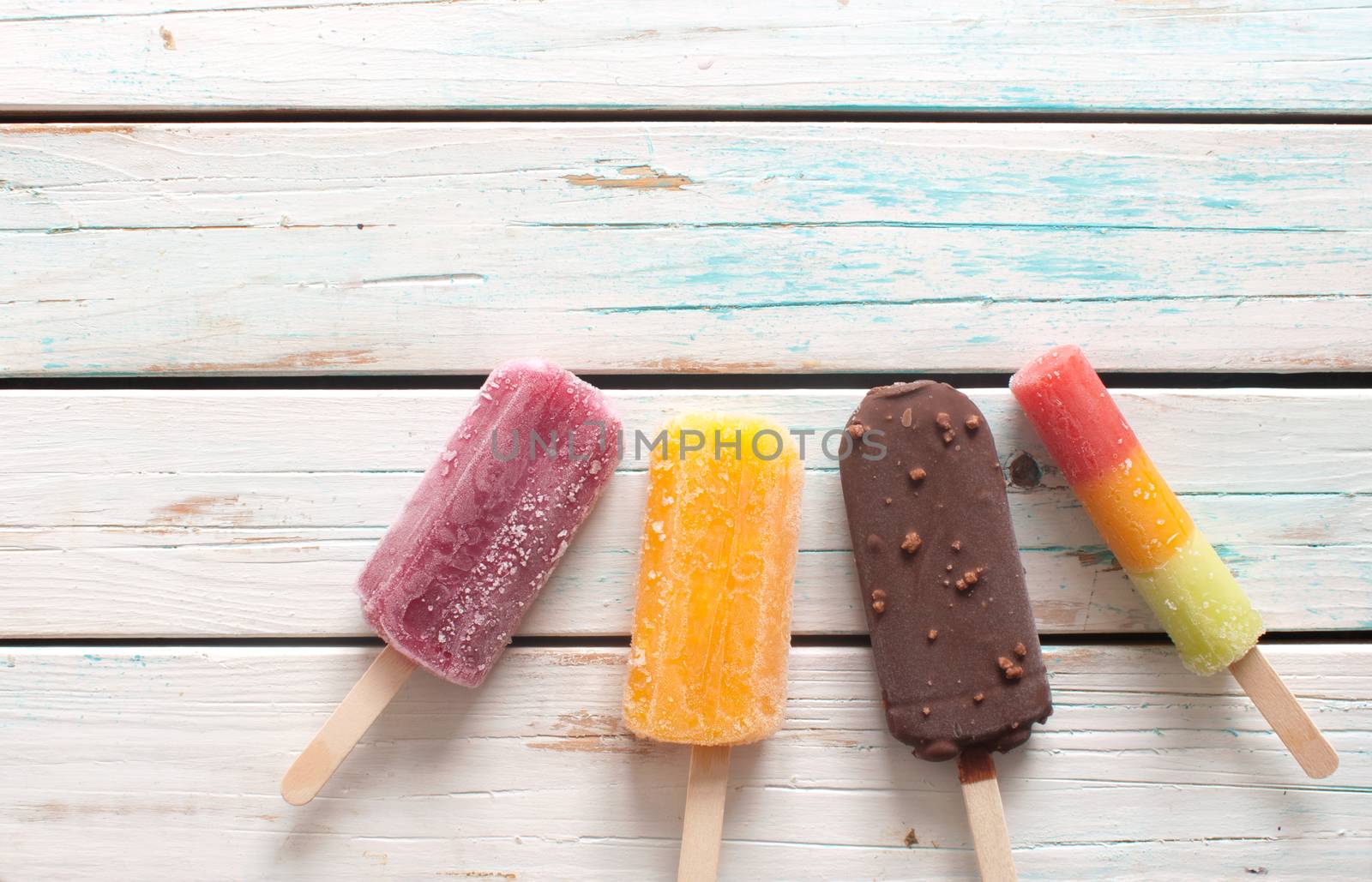 Various flavored ice popsicles over wooden background