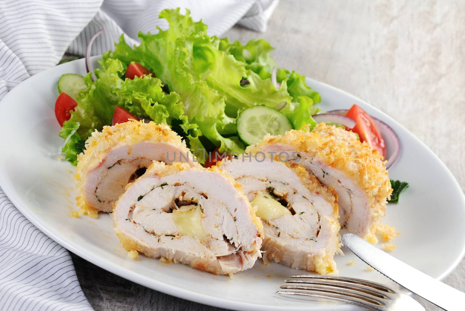 Sliced baked until golden, crispy crust chicken roll in breadcrumbs with Parmesan cheese, stuffed with cheese with herbs and garnish of vegetables.