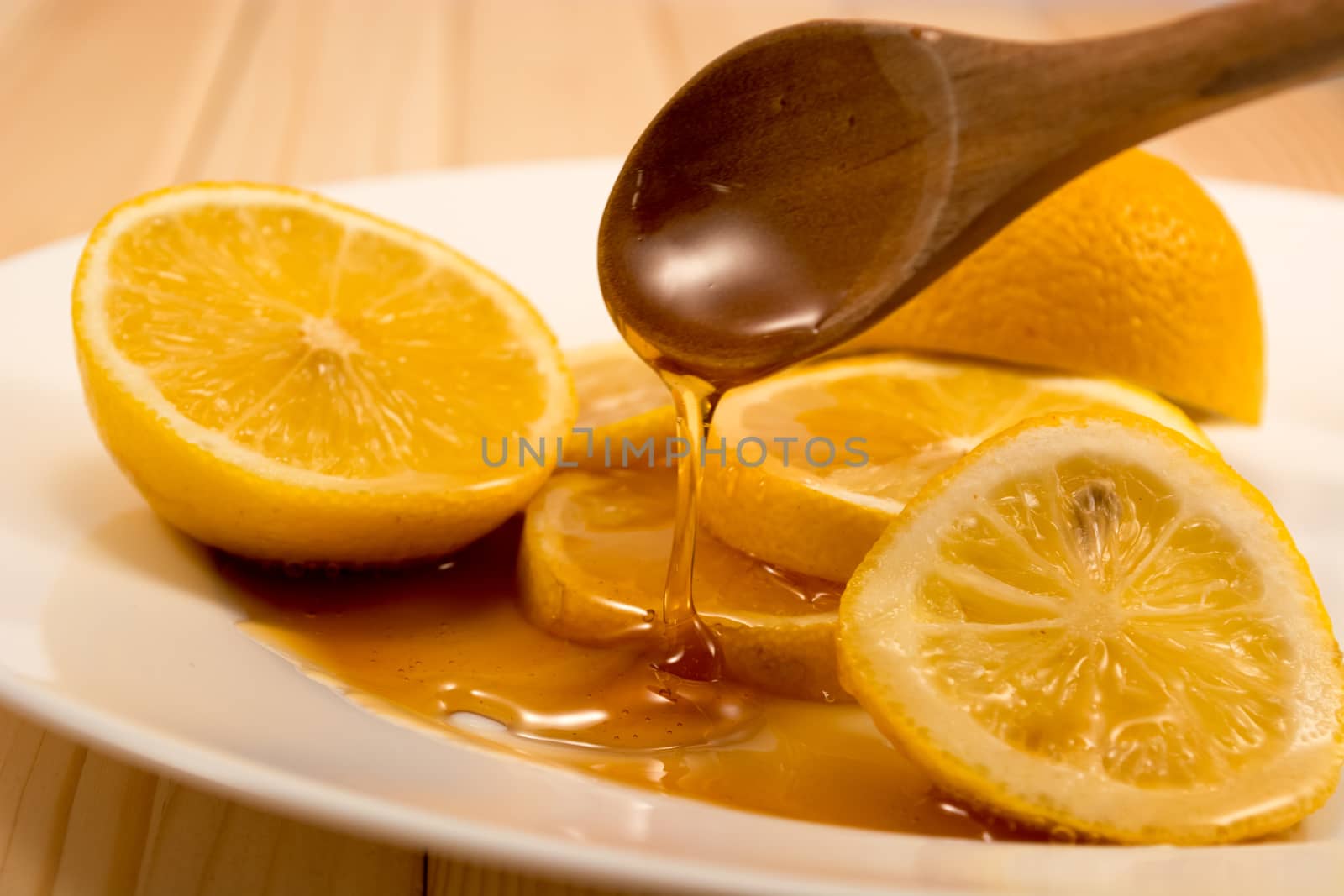 Closeup of sliced lemon and wooden spoon with honey on a plate
