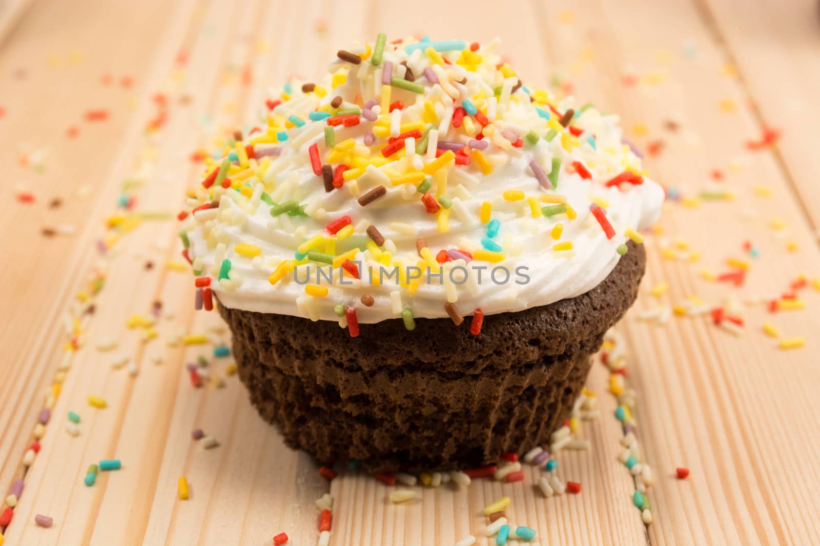 Muffin with cream and colorfull crumbs on top of it sitting on bright wooden table