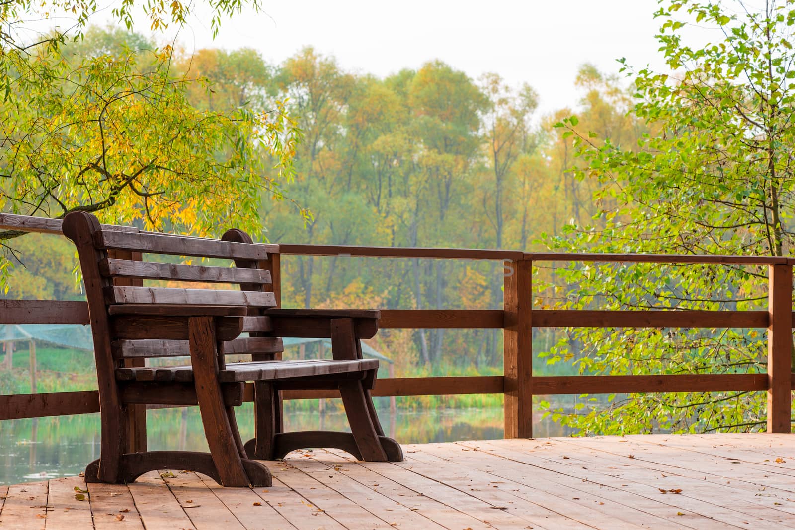 Wooden bench on a bridge over a lake in an autumn park by kosmsos111