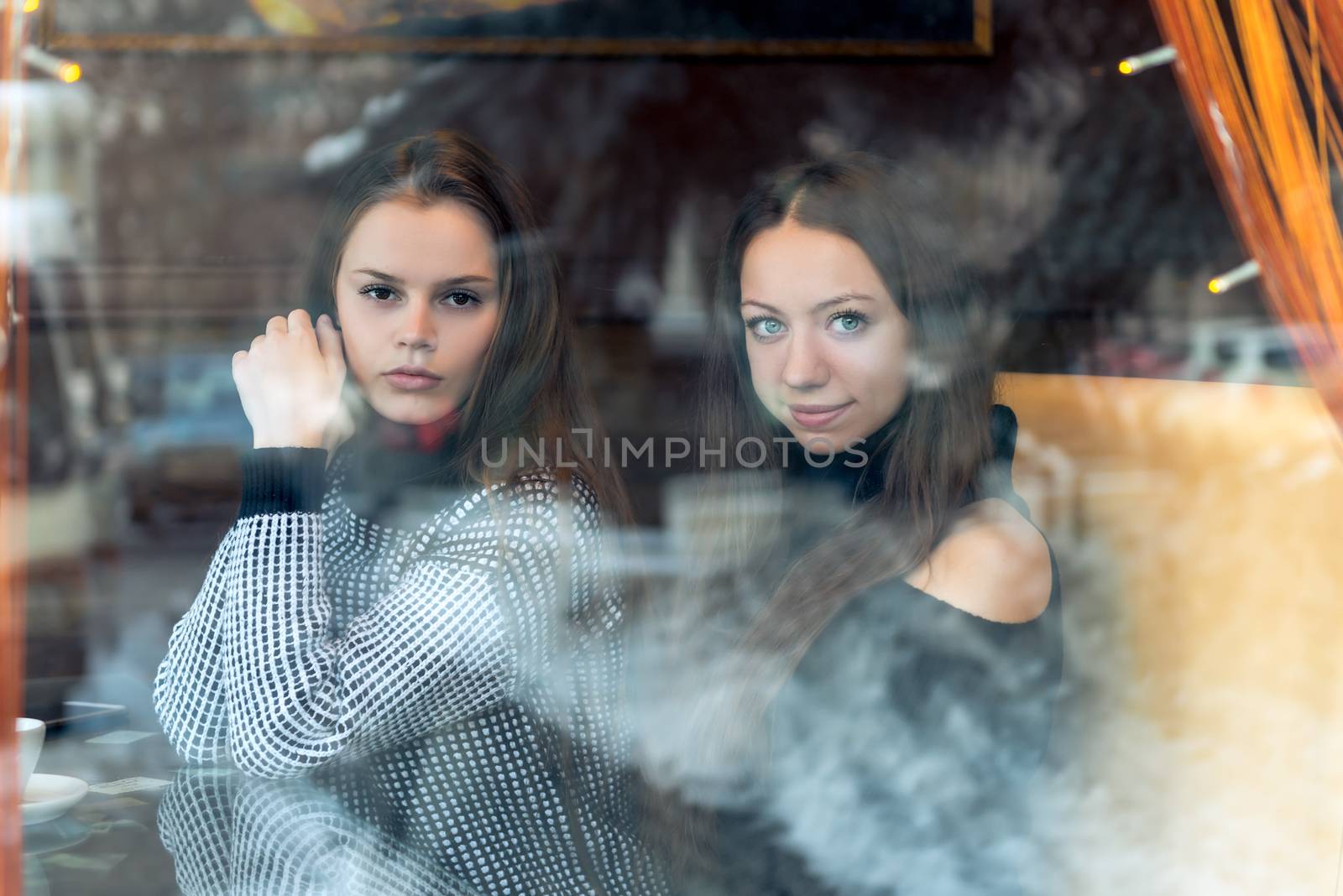 Portrait of young beautiful girlfriends in a cafe, shooting behind a glass