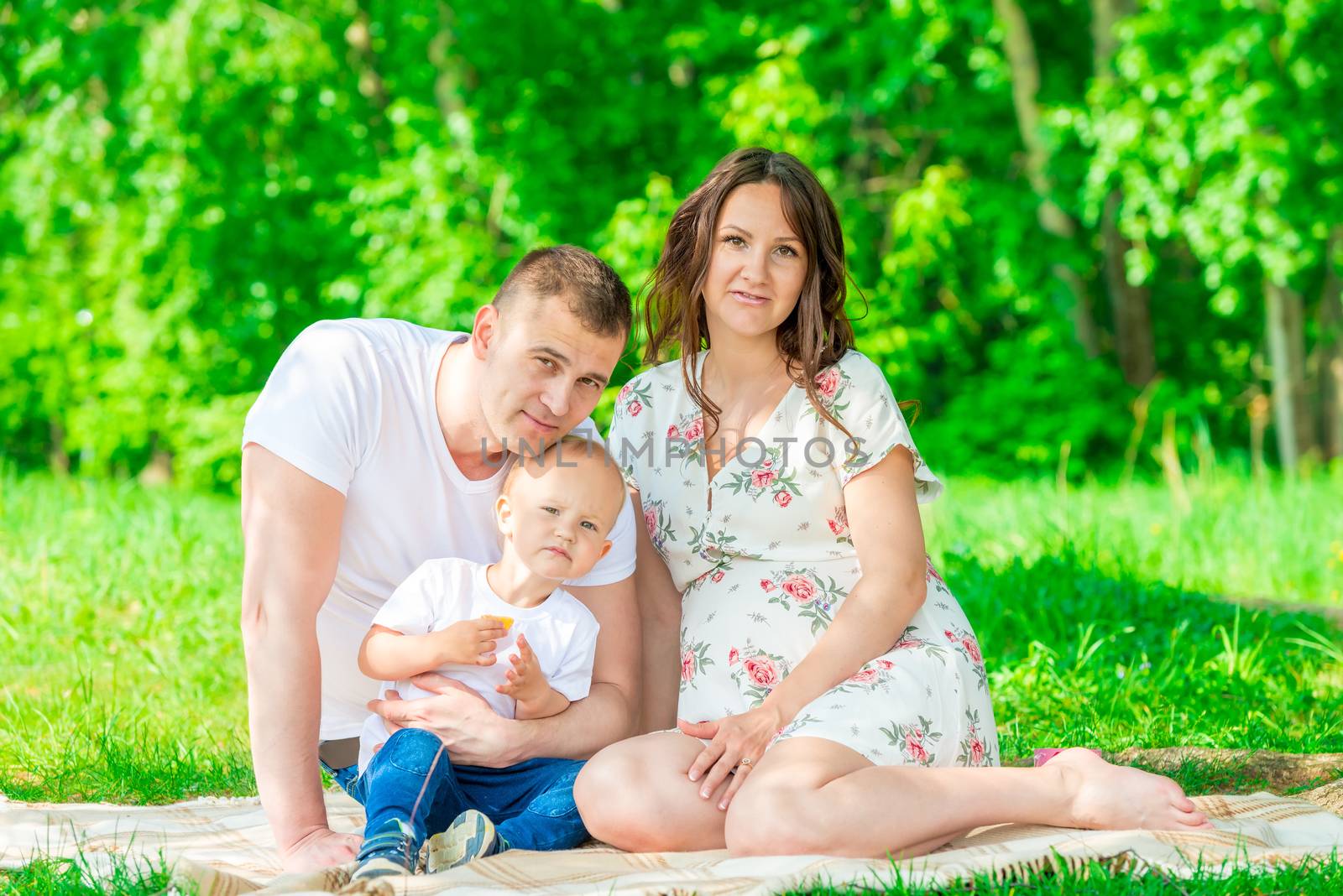 portrait of a young happy family in anticipation of a baby, shooting in a summer park