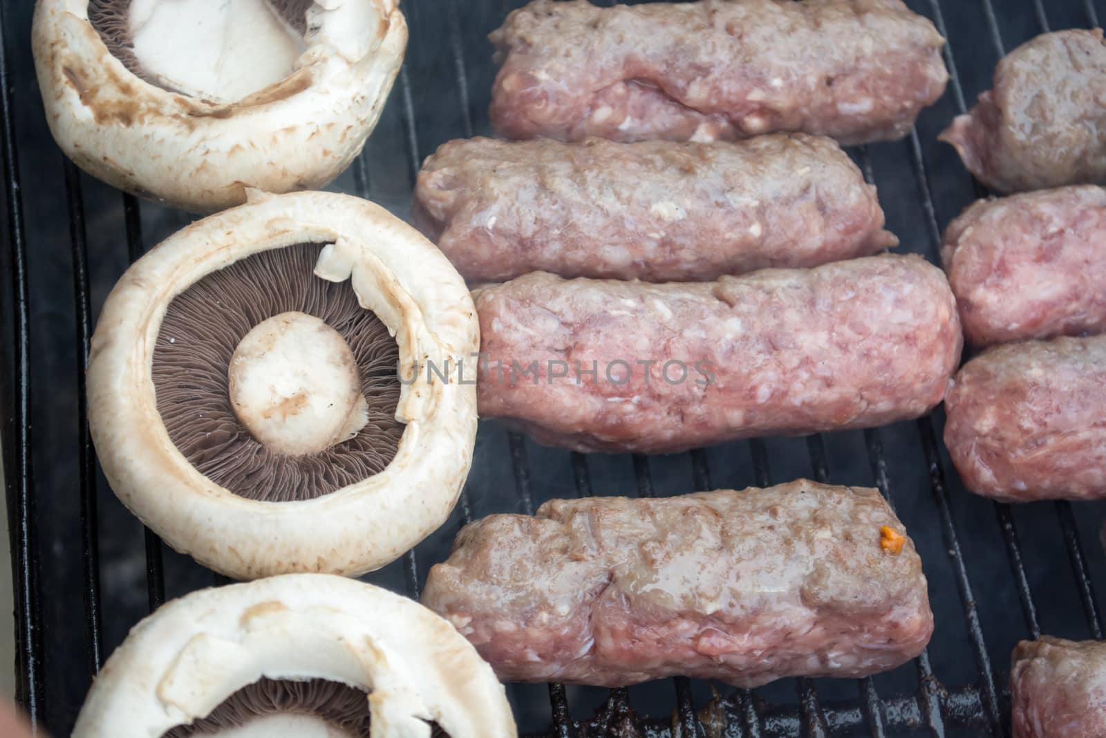 Grilling cevapi and mushrooms. Smoke visible. Upper angle